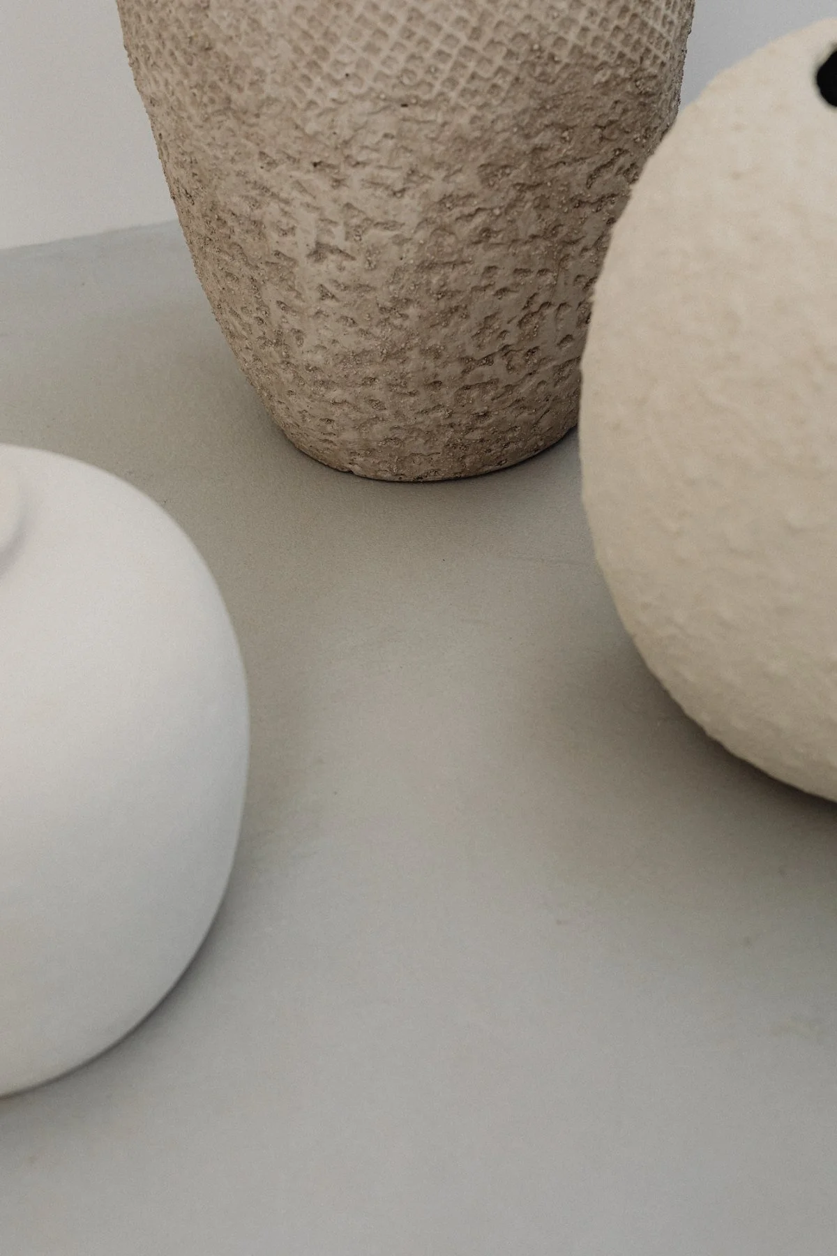 Close-up image of three minimalist objects with textured and smooth surfaces on a neutral background.