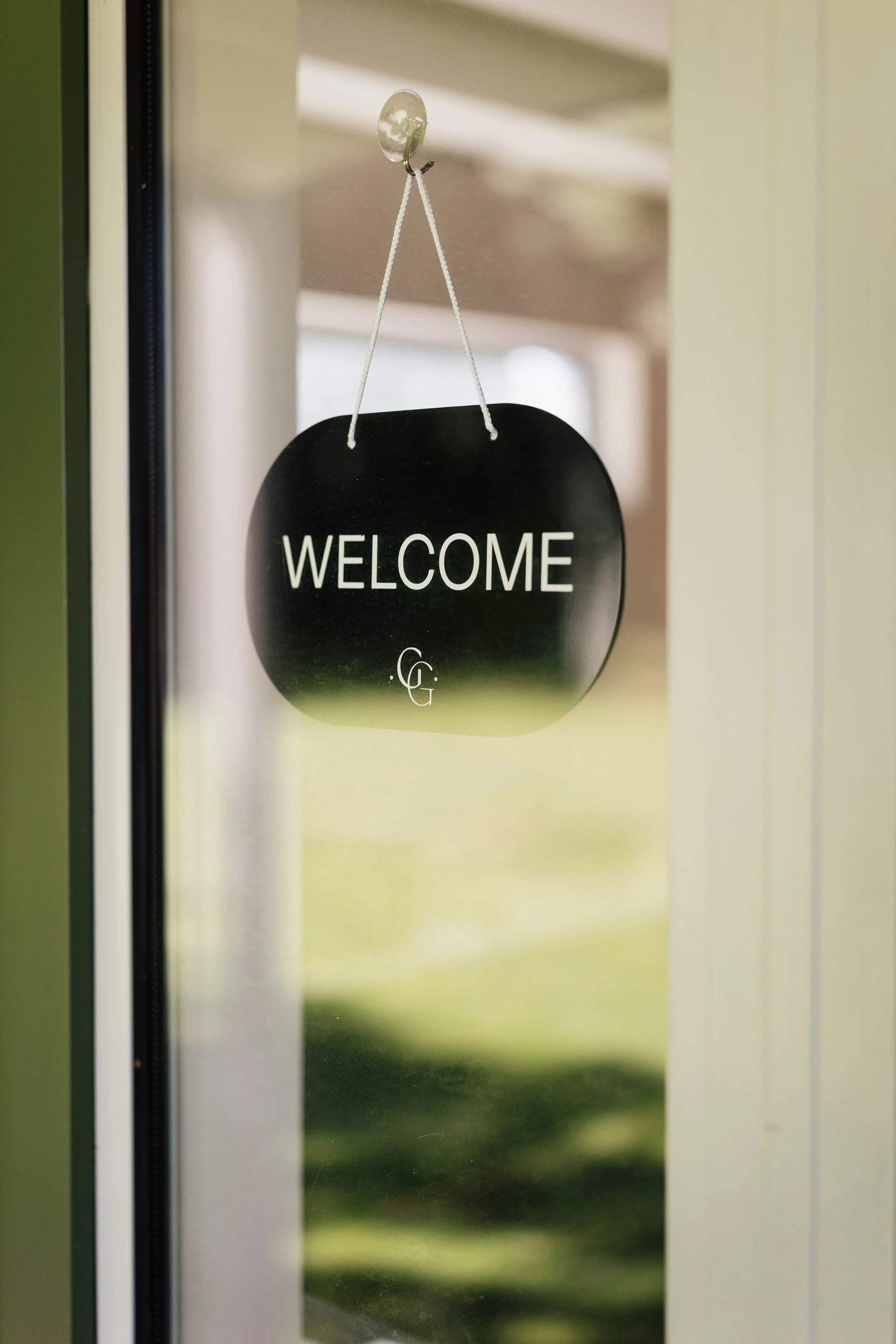 A door hanging sign with a black background and the word "WELCOME" in white, attached by a white string to a hook on a door.
