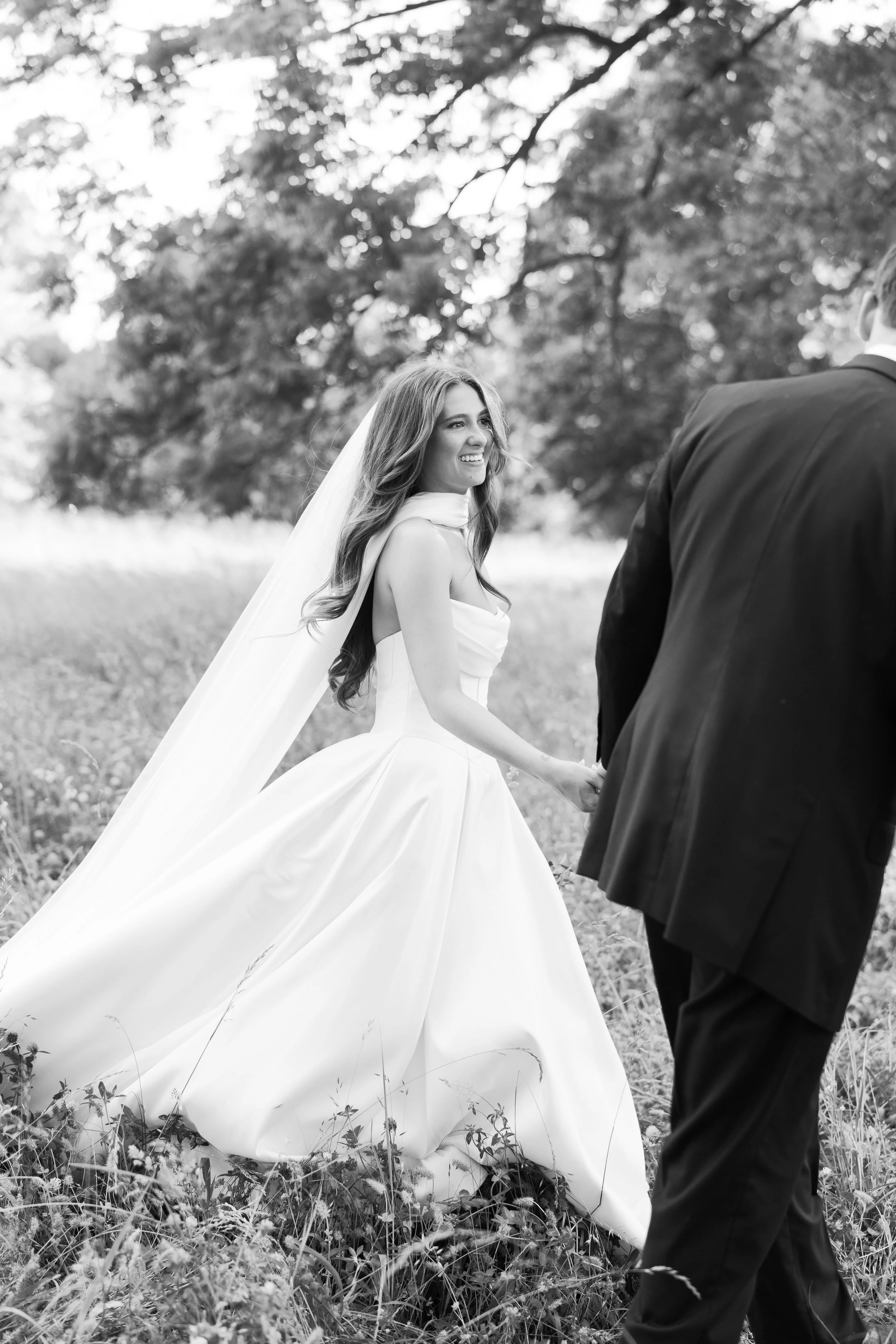 Bride laughing and looking back at groom during wedding portrait session in open field, West Tennessee wedding photographer