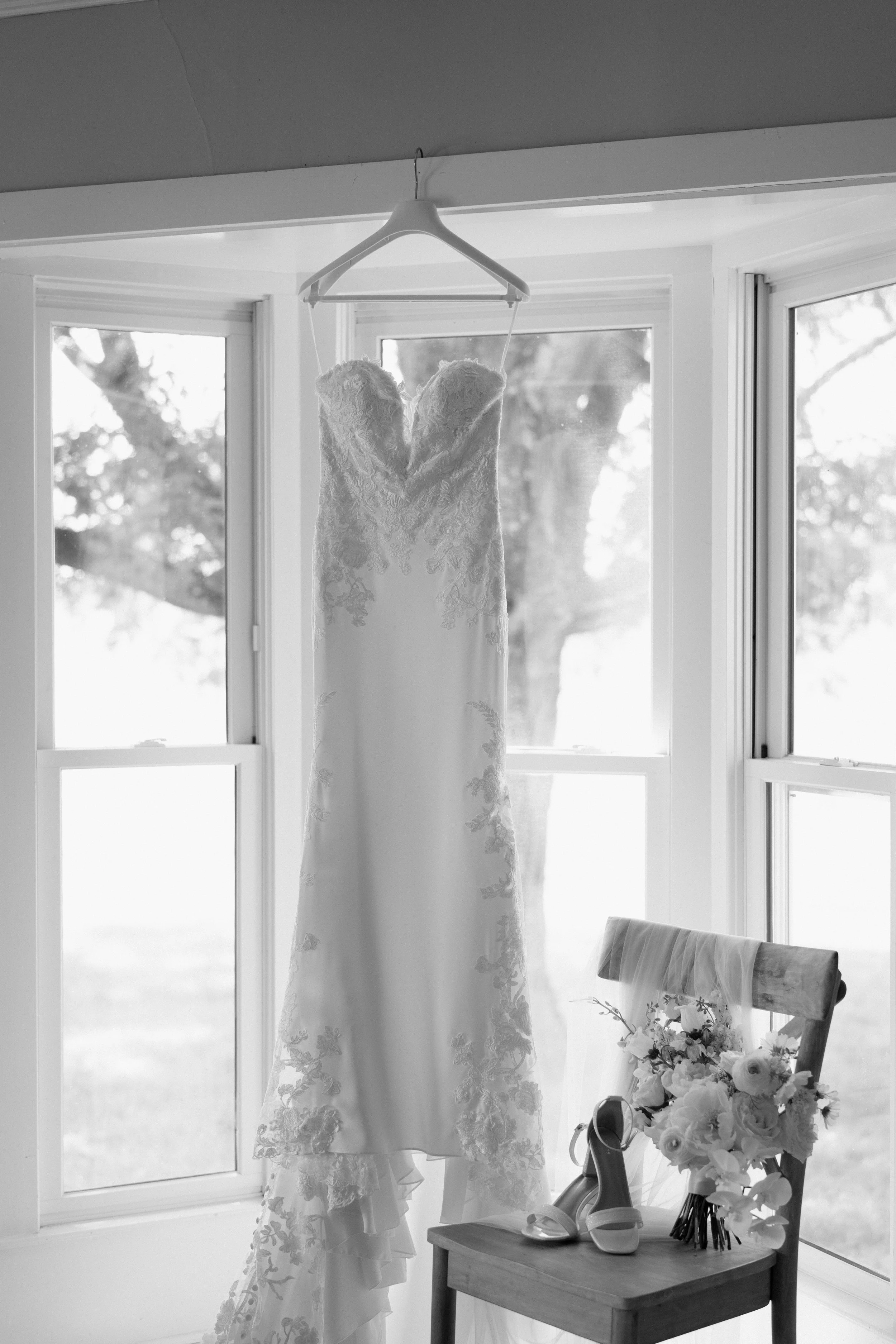Wedding gown hanging in window light with bridal bouquet on chair, Tennessee wedding photographer