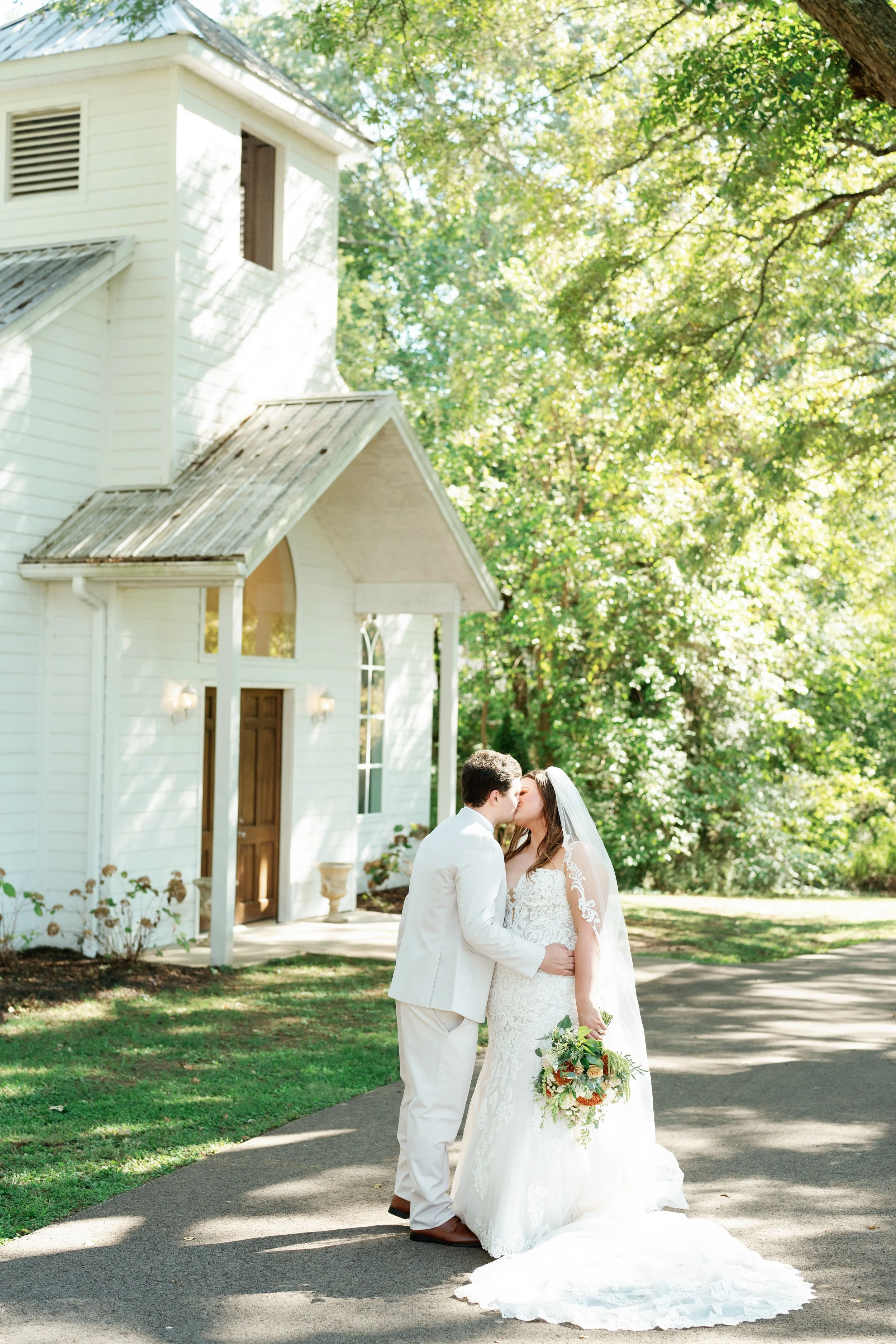 Bride and groom sharing a kiss in front of the white outdoor wedding chapel at The Venue at Twin Oaks in Humboldt Tennessee