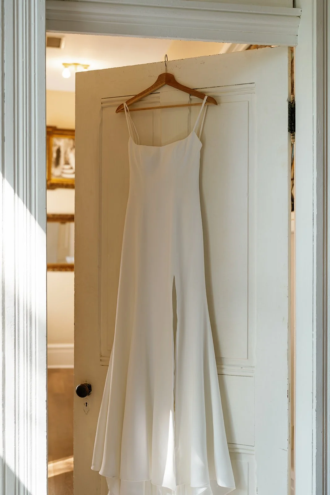 A white wedding dress hanging on a wooden hanger on a door.