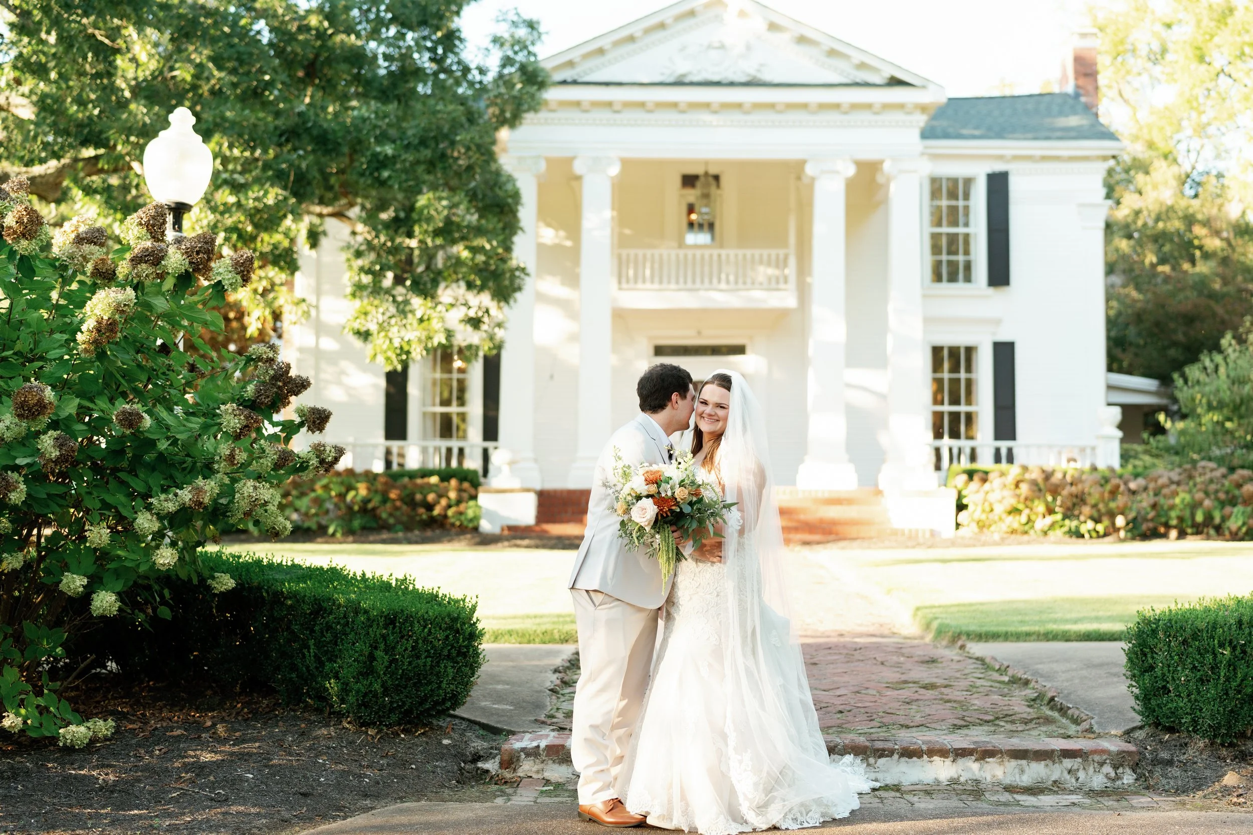 Bride and groom portrait in front of the antebellum mansion at The Venue at Twin Oaks in Humboldt Tennessee during golden hour with hydrangeas in the foreground