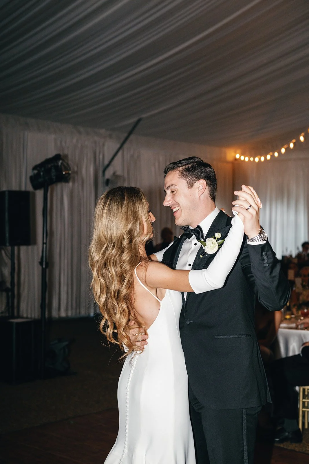 A bride and groom dancing at their wedding reception in a decorated tent.