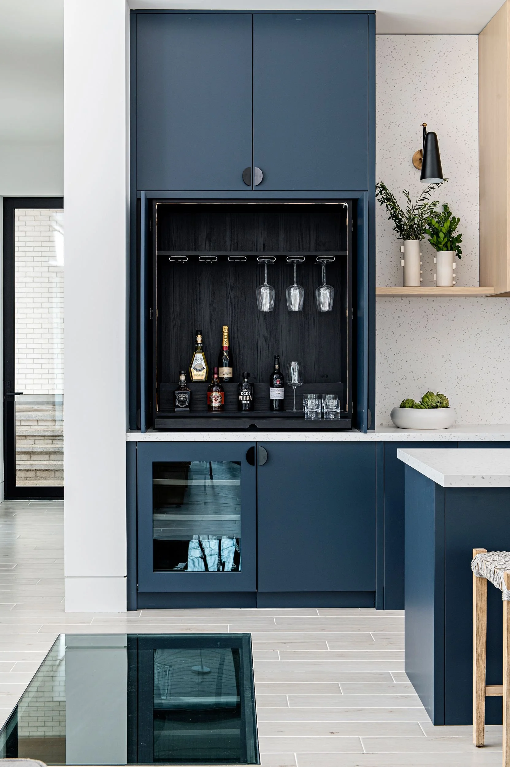 Blue built-in bar cabinet with glassware and liquor bottles, located in a modern kitchen or living area.