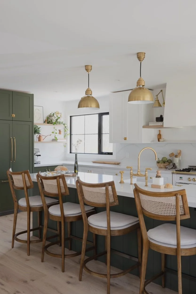 Modern kitchen with green cabinets, white countertops, and gold fixtures, featuring a kitchen island with four wooden chairs.