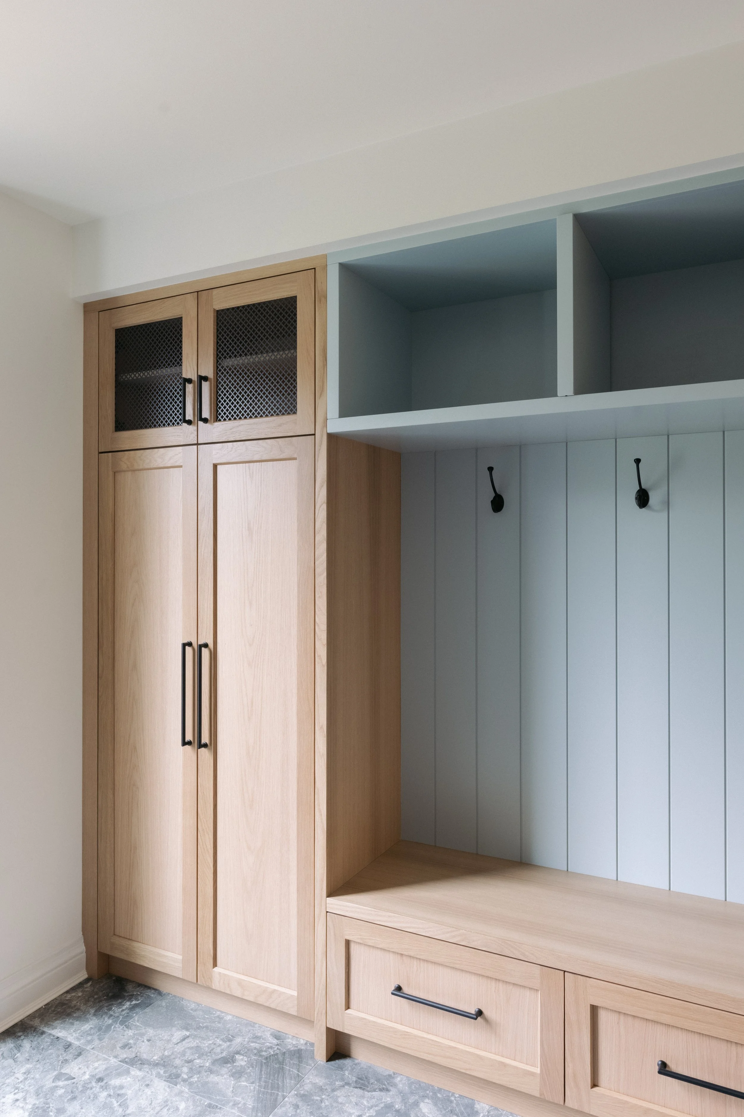 Close-up of a built-in wooden cabinet with black handles, a bench area with two drawers, and open shelving above, in a modern home interior.