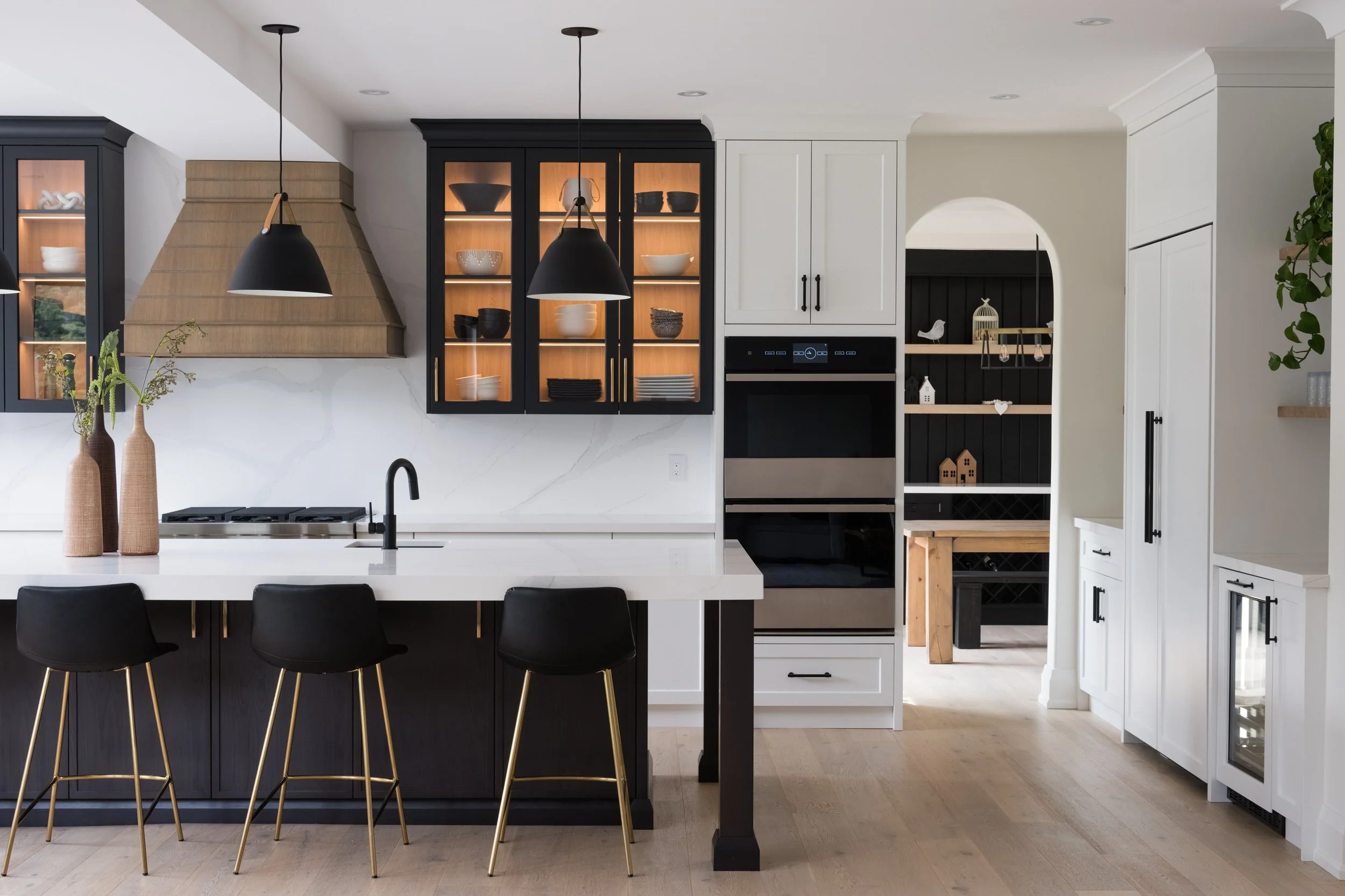 Modern kitchen with black and white cabinetry, black pendant lights, a large white island with three black chairs, and open shelving with decorative items.
