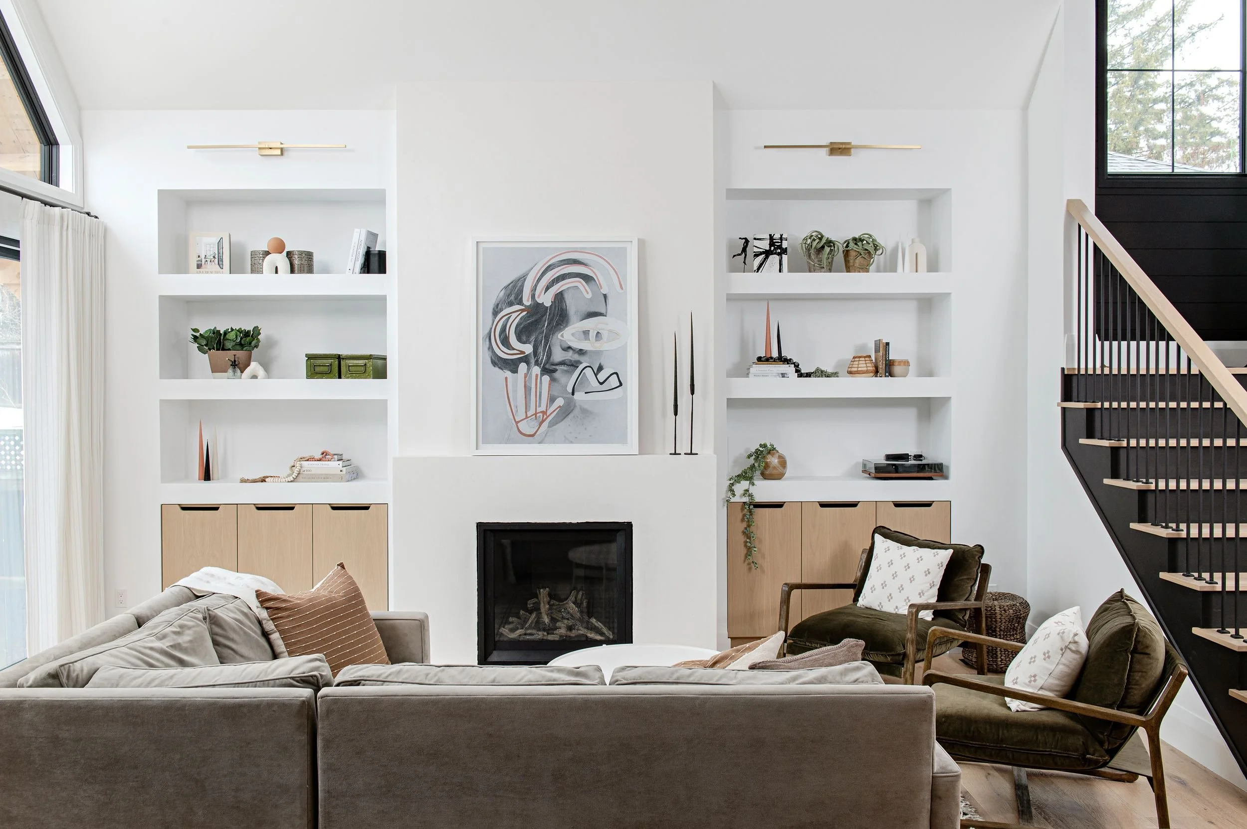 Living room with white walls, built-in shelves, a fireplace, and contemporary furniture, including a beige sofa and two wooden chairs with cushions.