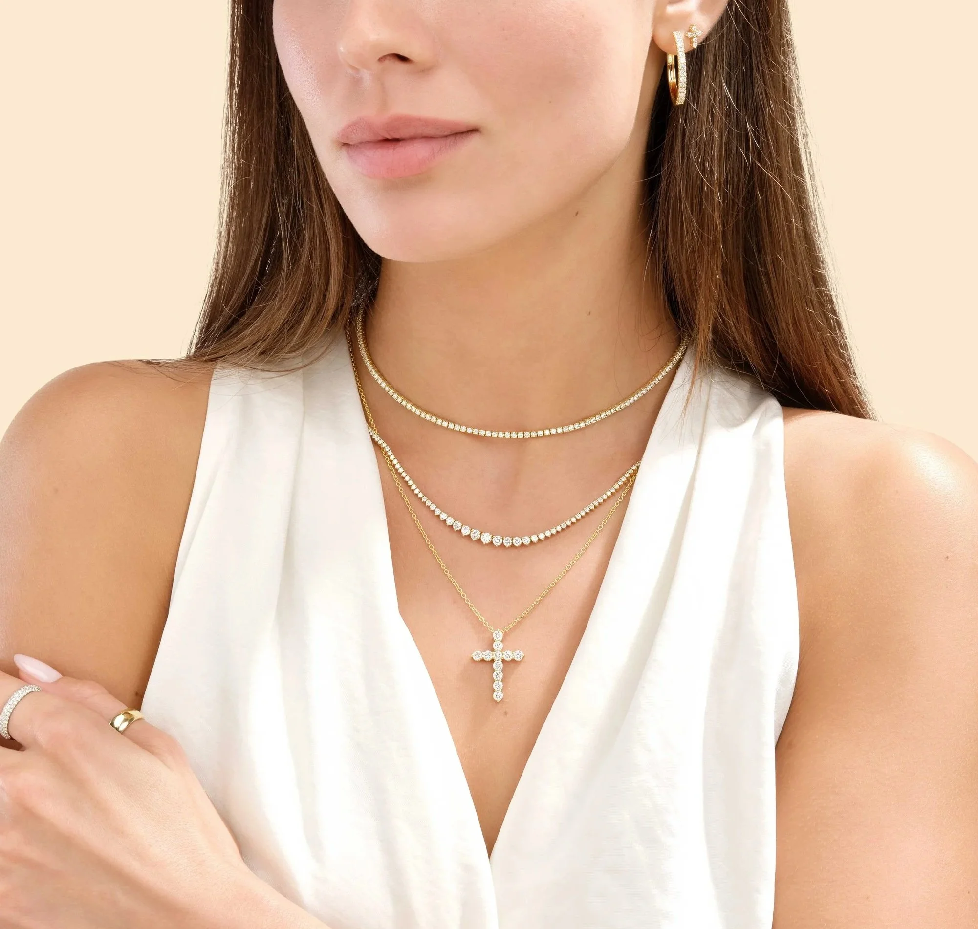 Close-up of a woman wearing multiple gold and diamond necklaces, earrings, and rings, with a white sleeveless top and natural makeup.