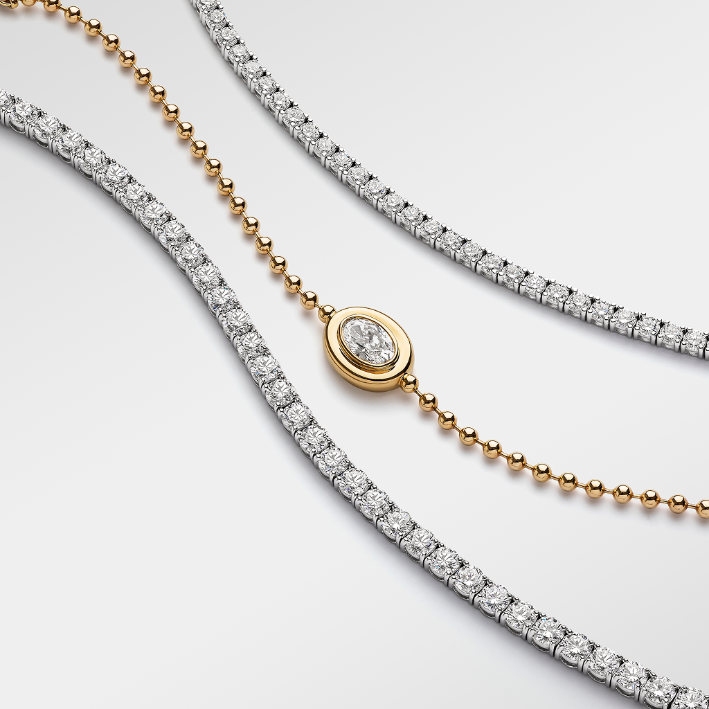 Three elegant necklaces laid out on a white background: one with a series of diamonds, one with gold beads, and a third with a halo diamond pendant.
