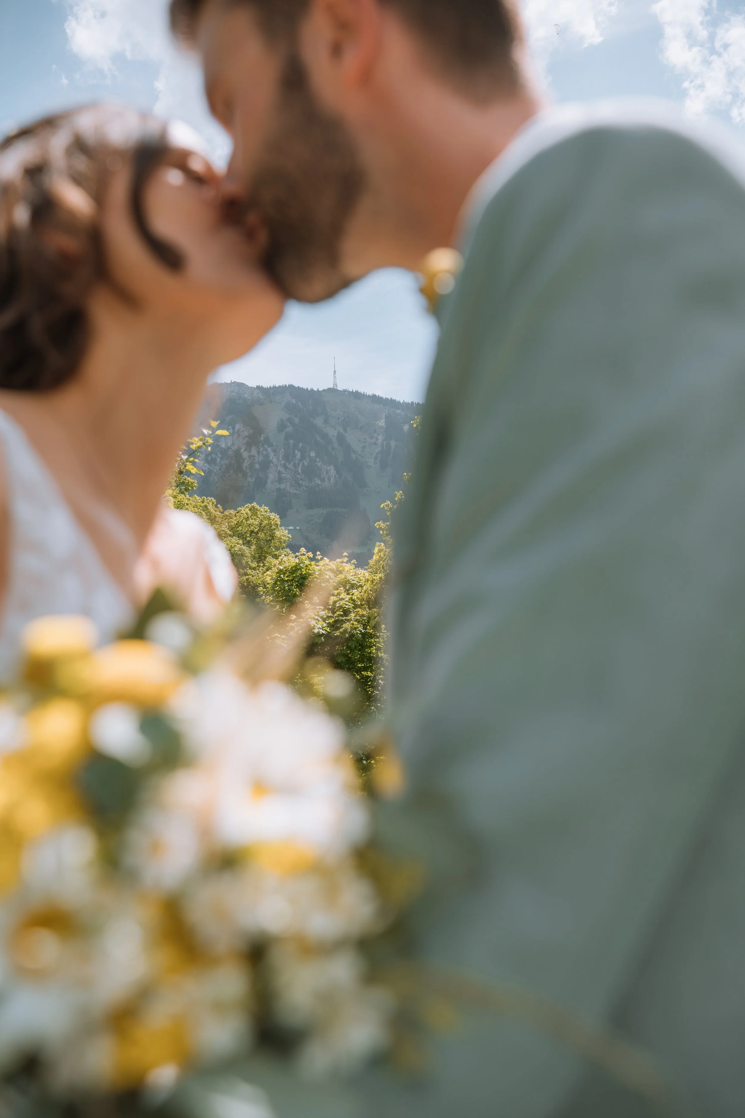 Ein Paar küsst sich bei Sonnenlicht im Freien, im Hintergrund sind Bäume und Berge sichtbar.