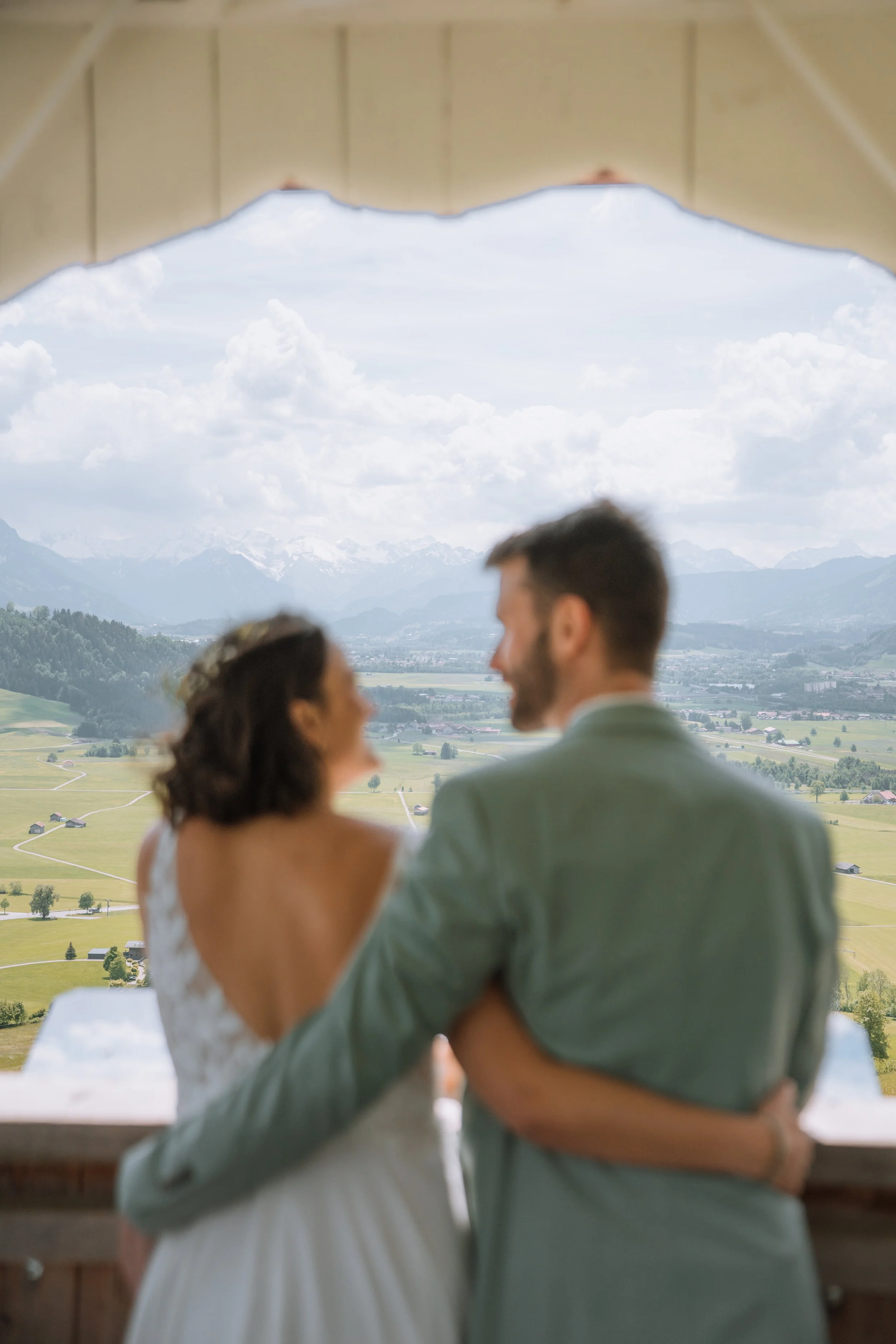 Verliebtes Paar am Fenster mit Berg- und Landschaftsblick, Rückenansicht, Hochzeitskleid und Anzug