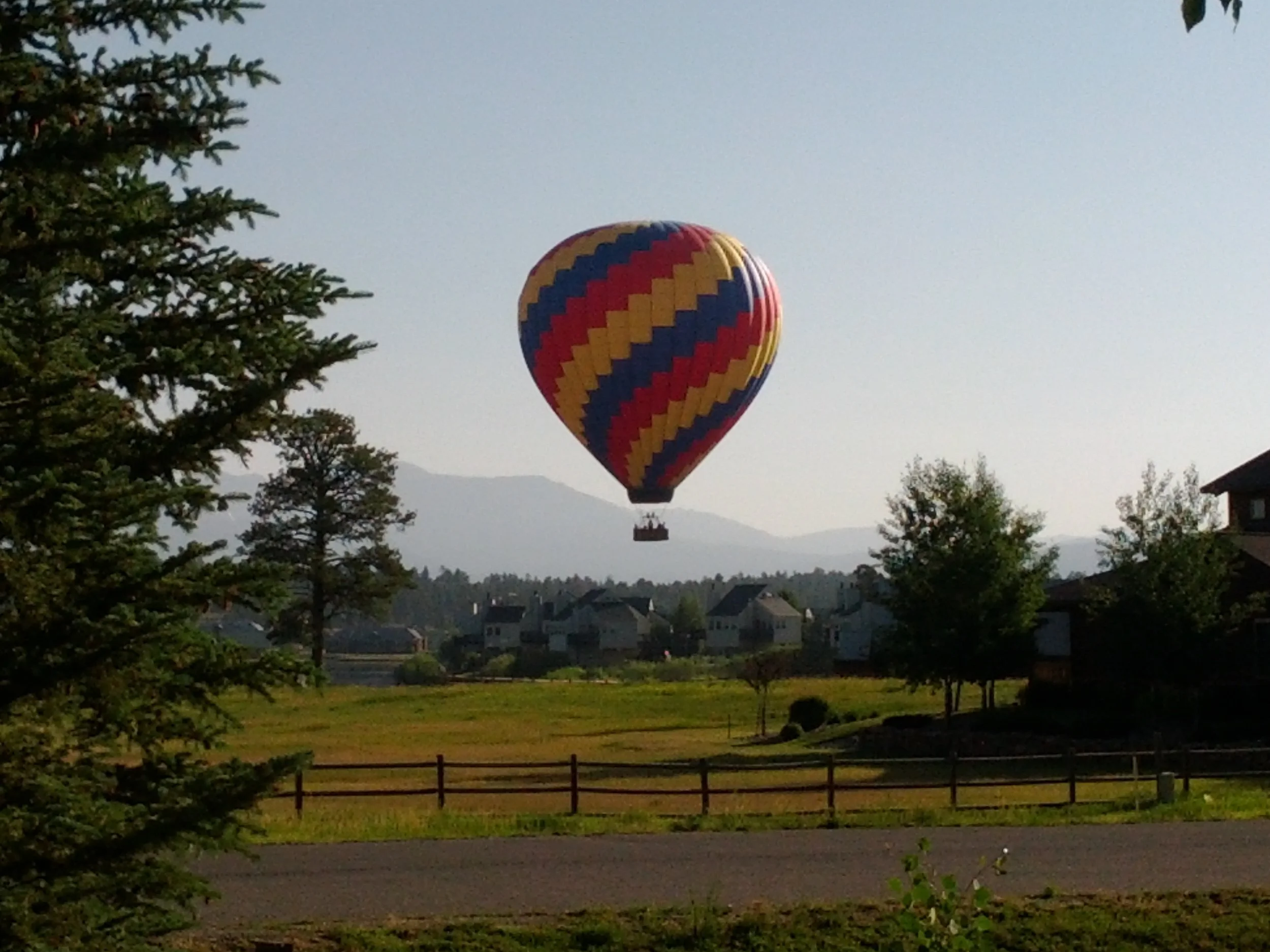 Colorful hot air balloon flying over Northern Virginia with houses, trees, and mountains in the background.