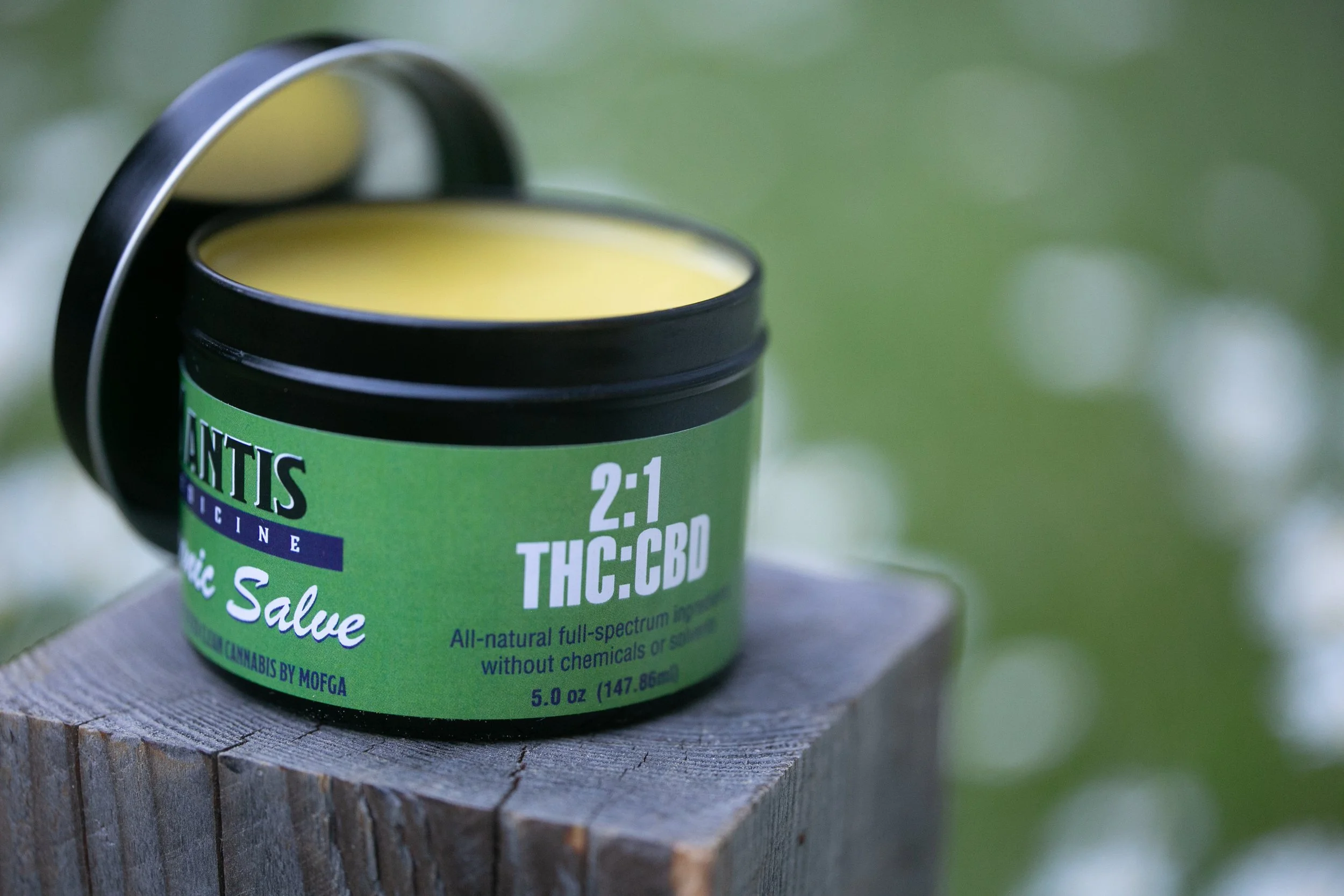 2:1 THC:CBD topical salve on a wooden surface with green grass background.