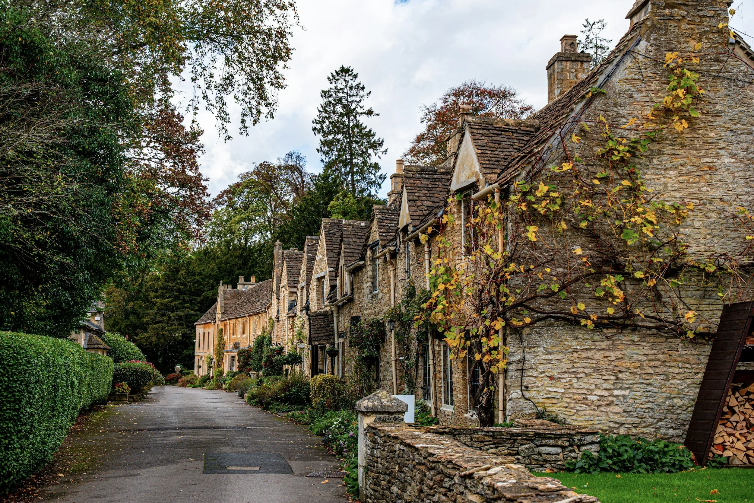 A street view with stone houses and lush greenery in a small village, autumn season, cloudy sky.