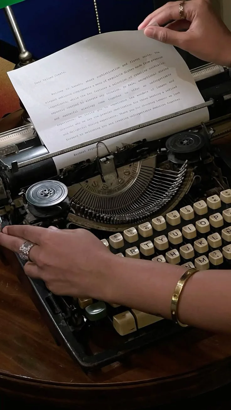 Close-up of a vintage typewriter with a typed letter and a person's hands adjusting the paper and typing. The person is wearing rings and a bracelet.