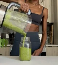 Woman pouring green smoothie from blender into a glass jar