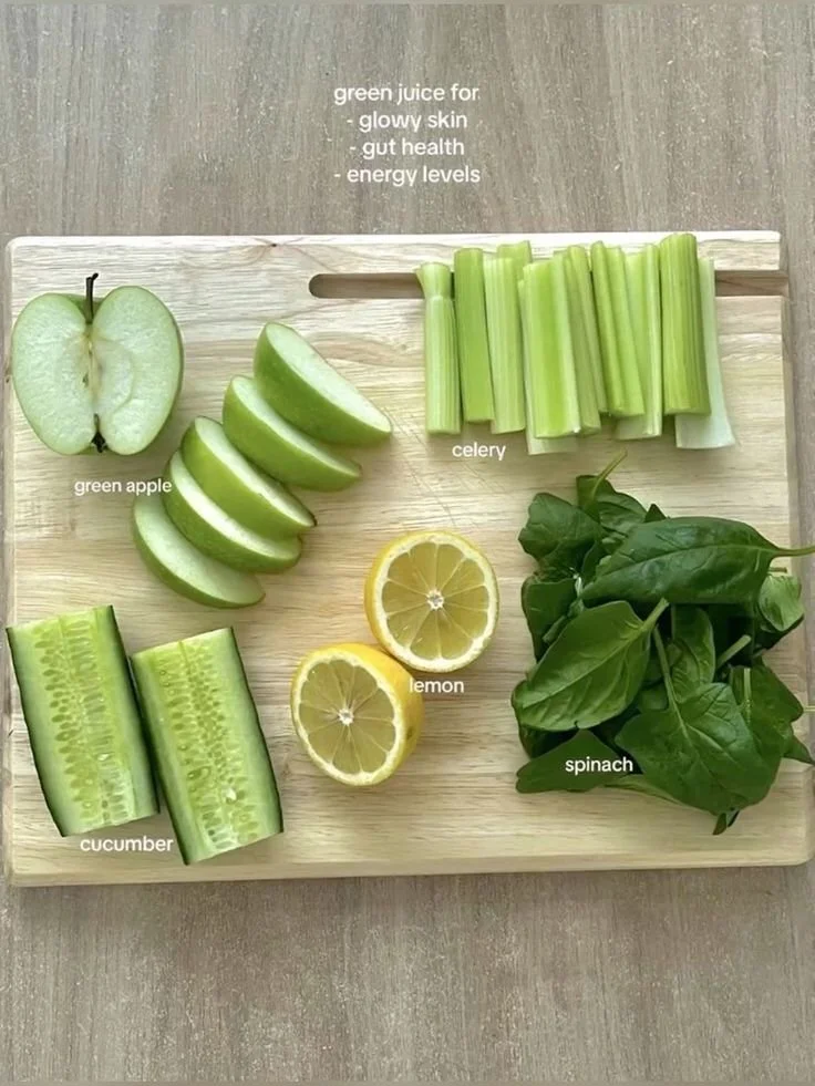 Sliced green apple, lime, cucumber, celery, and spinach leaves arranged on a wooden cutting board, with small labels for each item.