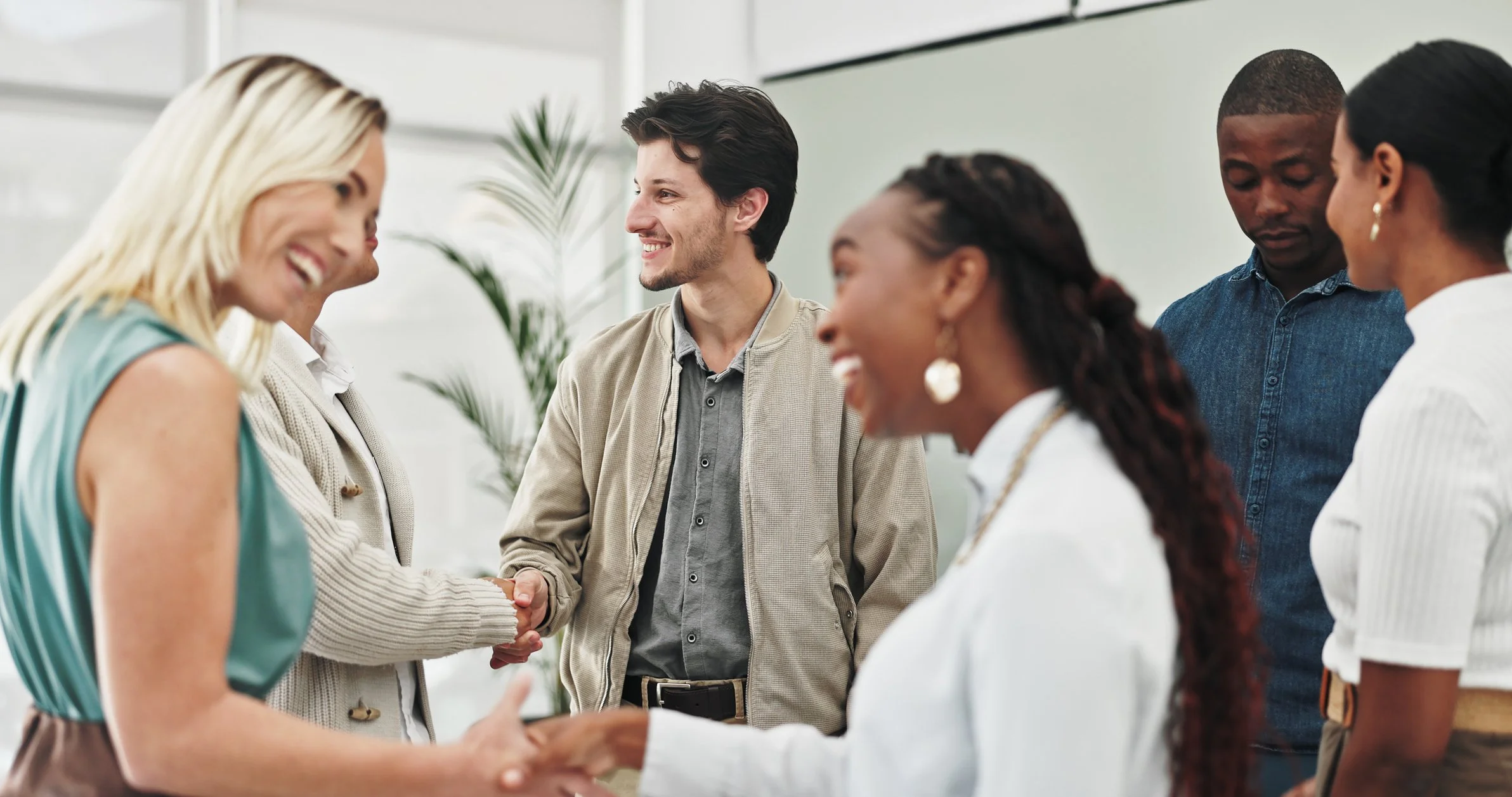 A group of diverse professionals in a modern office engaging in handshakes and conversations.
