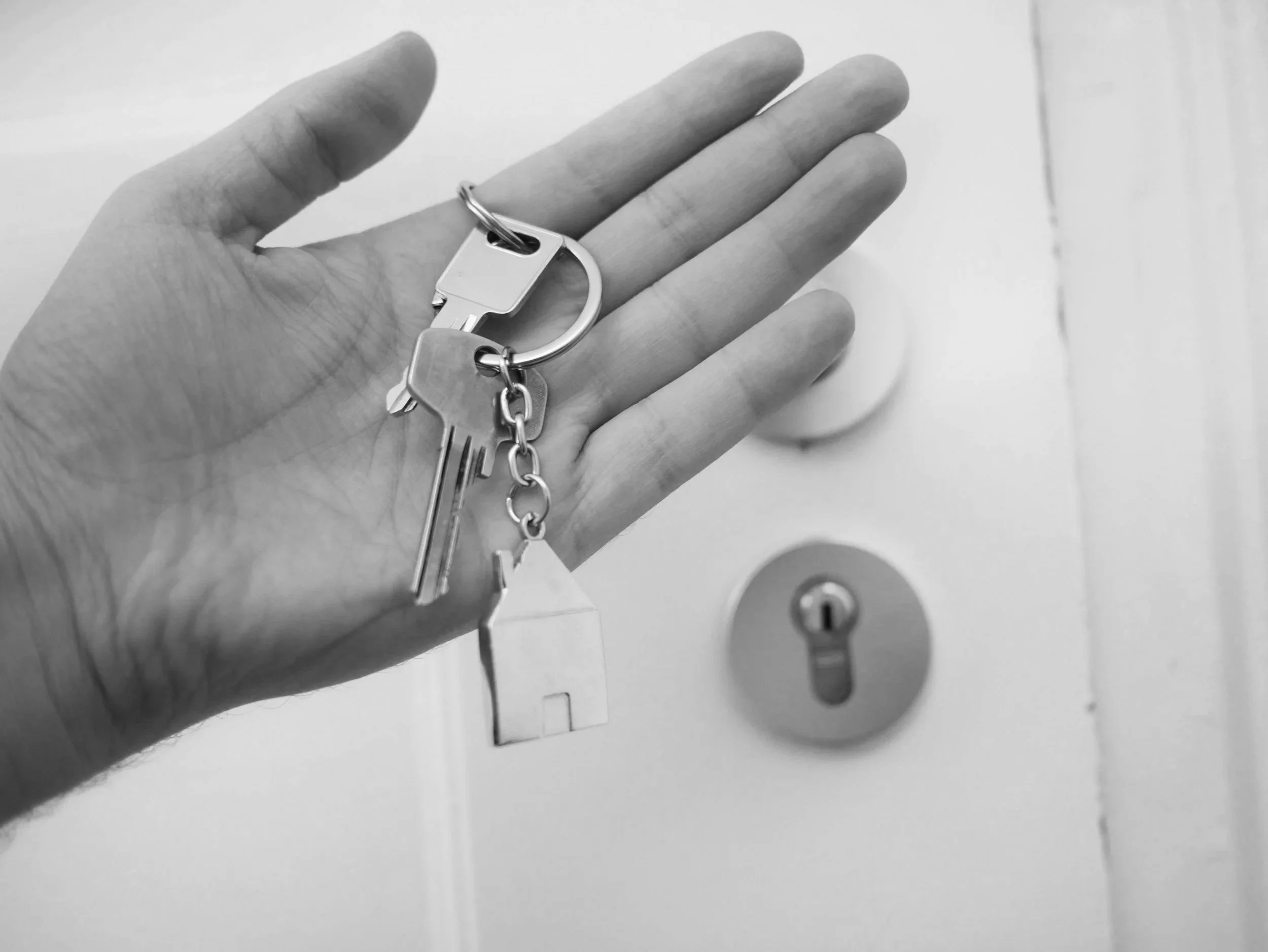 Hand holding keys with a house-shaped keychain in front of a door lock.