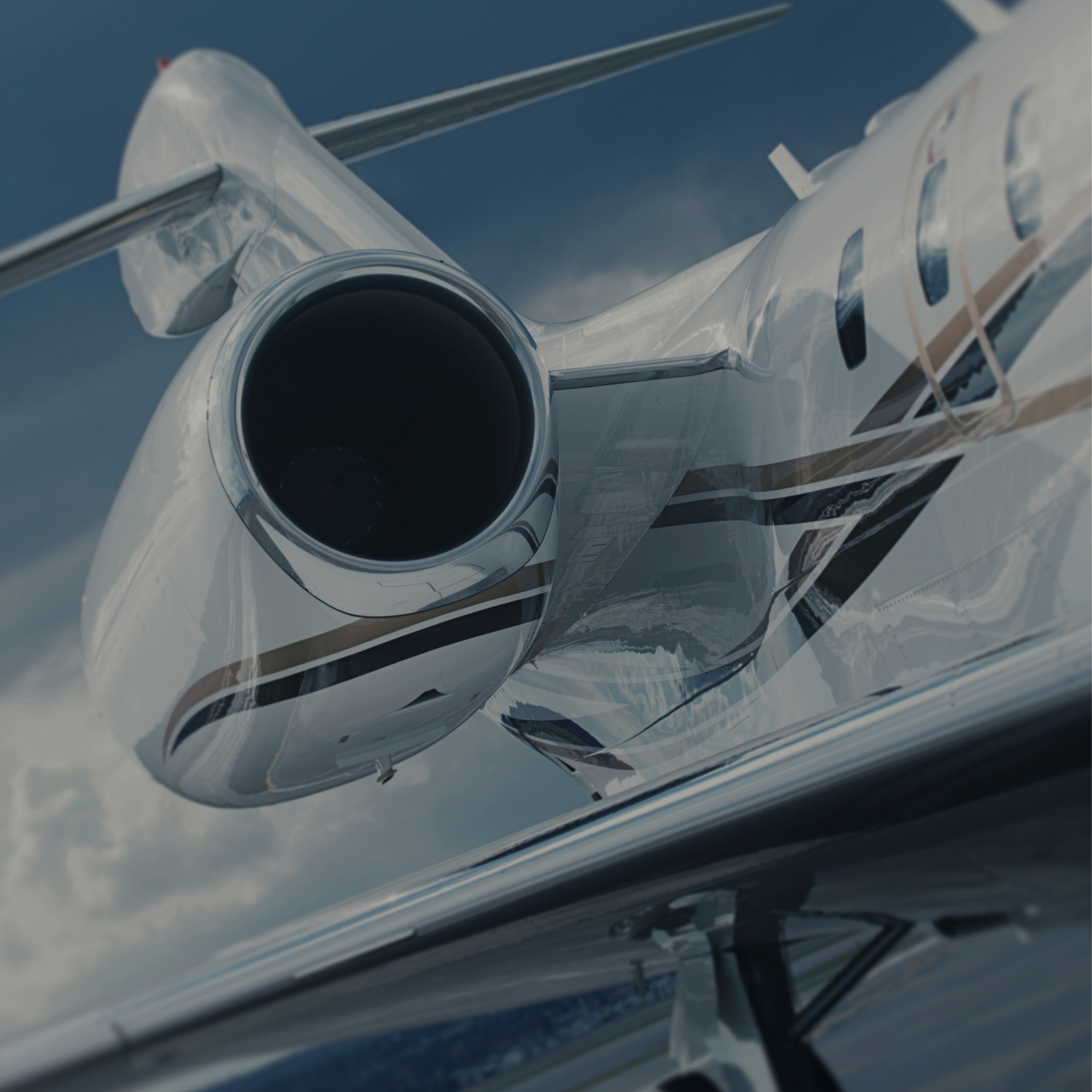 Close-up of a private jet's jet engine and wing against a cloudy sky.