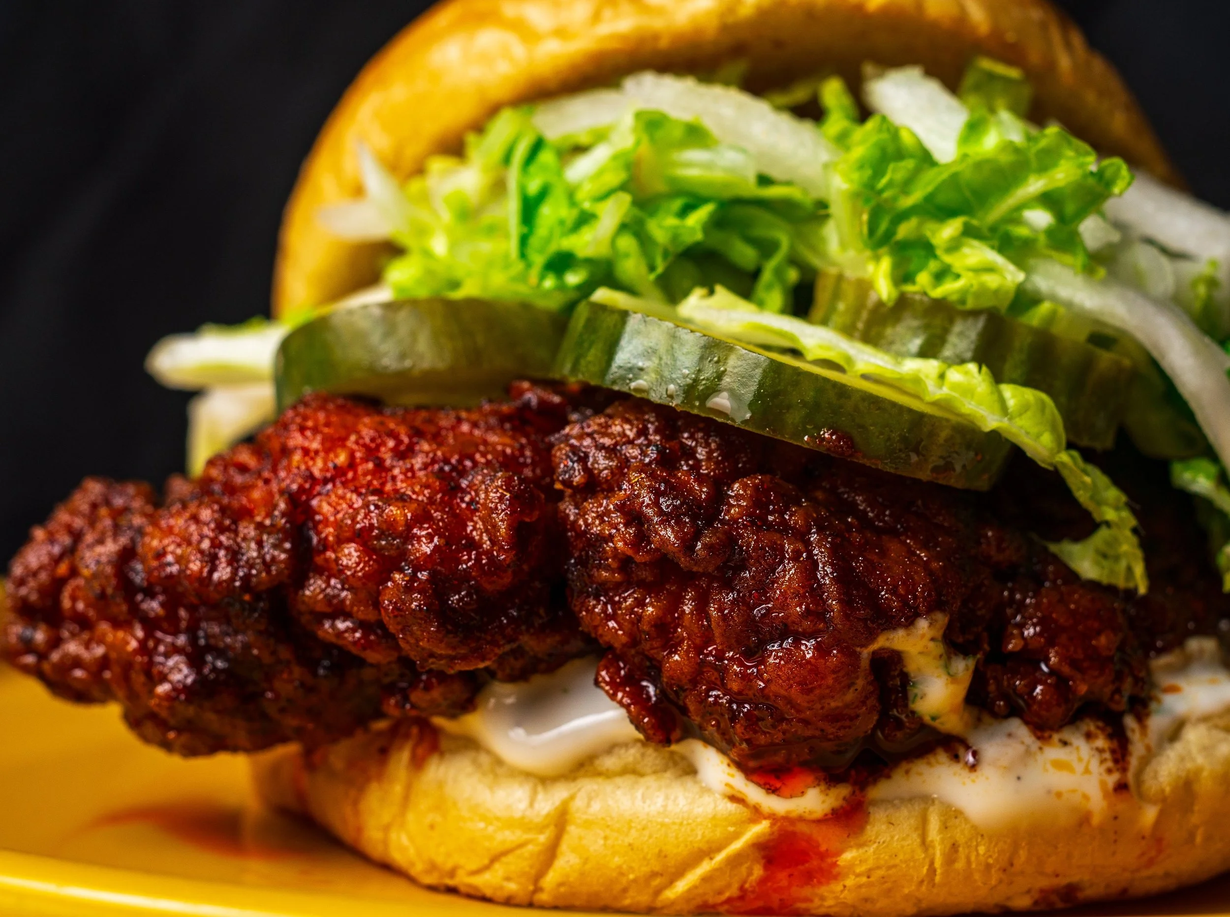 Un sándwich con pollo frito, rodajas de pepino, lechuga, cebolla y mayonesa en un bollo