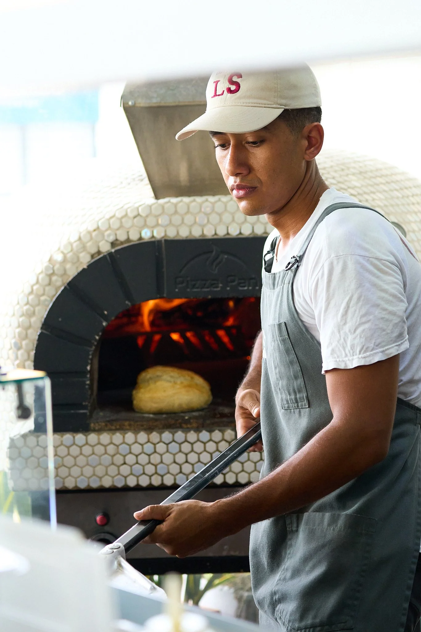 Joven pizzero sacando una pizza del horno de leña