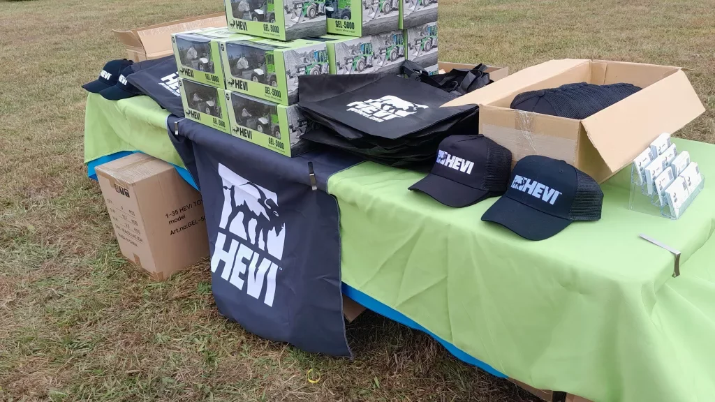 Table of event giveaway items, including a custom made table runner, hats, bags, business cards and scale models of an older wheel loader.