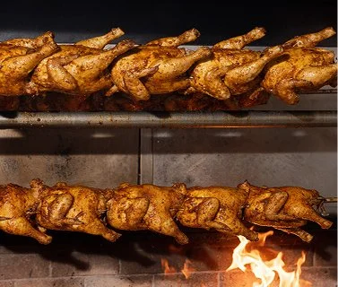 Two rows of rotisserie chickens cooking on a spit over an open flame.