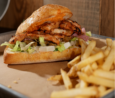Roasted chicken sandwich with lettuce, onions, and sauce in a ciabatta sandwich, served with French fries on a tray.