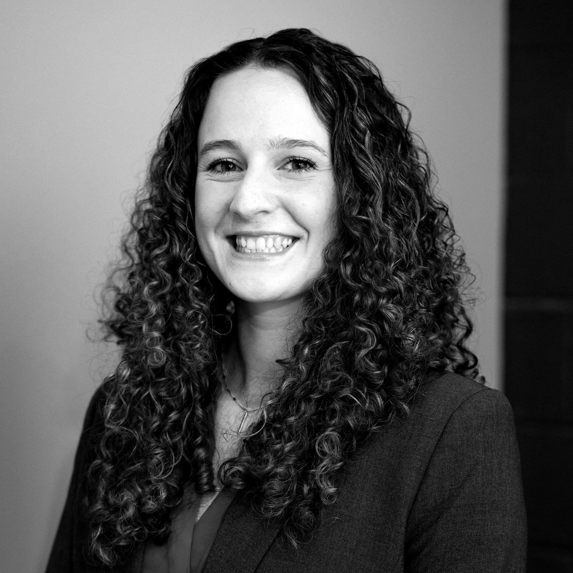 A smiling woman with curly hair wearing texted clothing against a plain background.