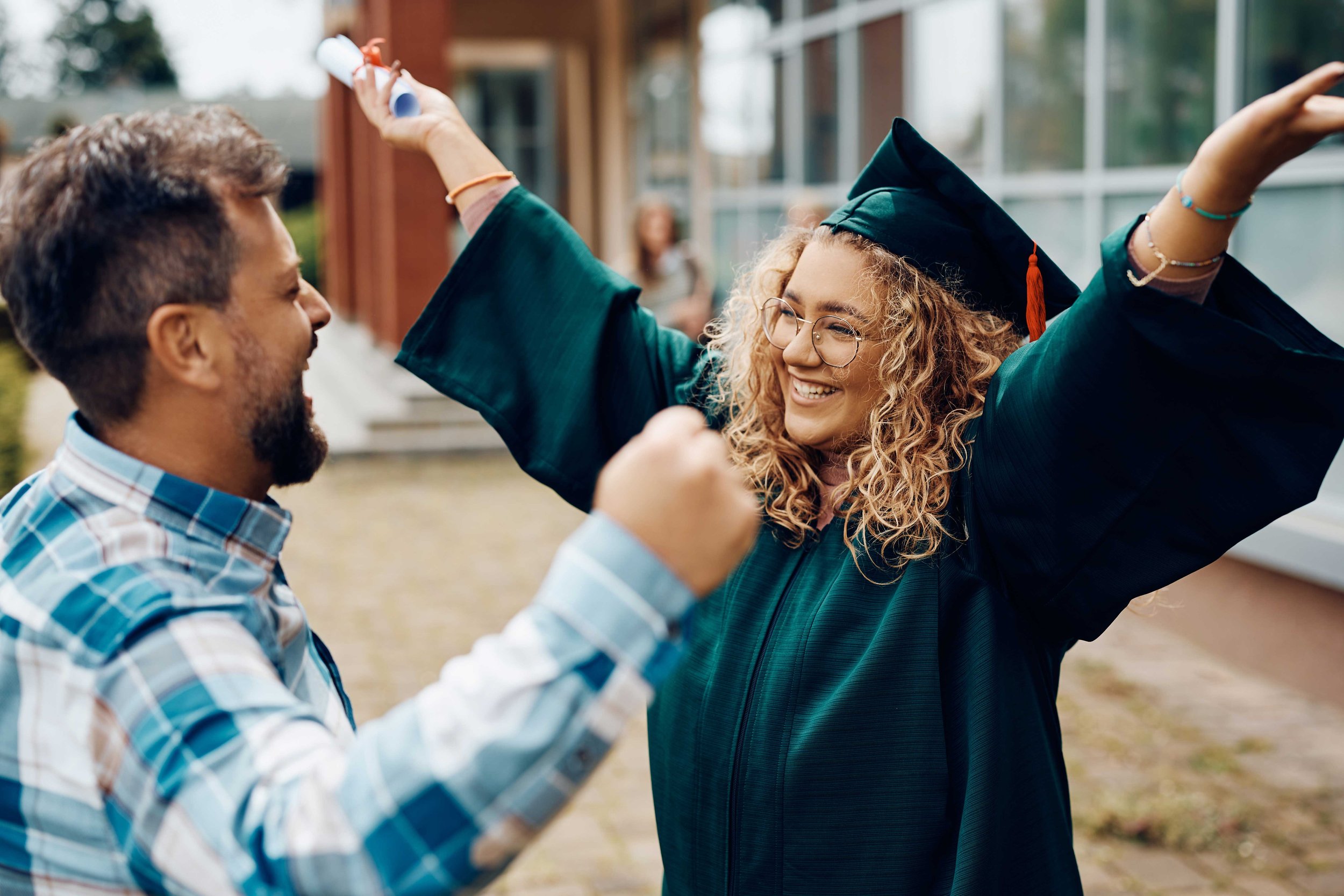 Student graduate in green gown and cap celebrating with dad