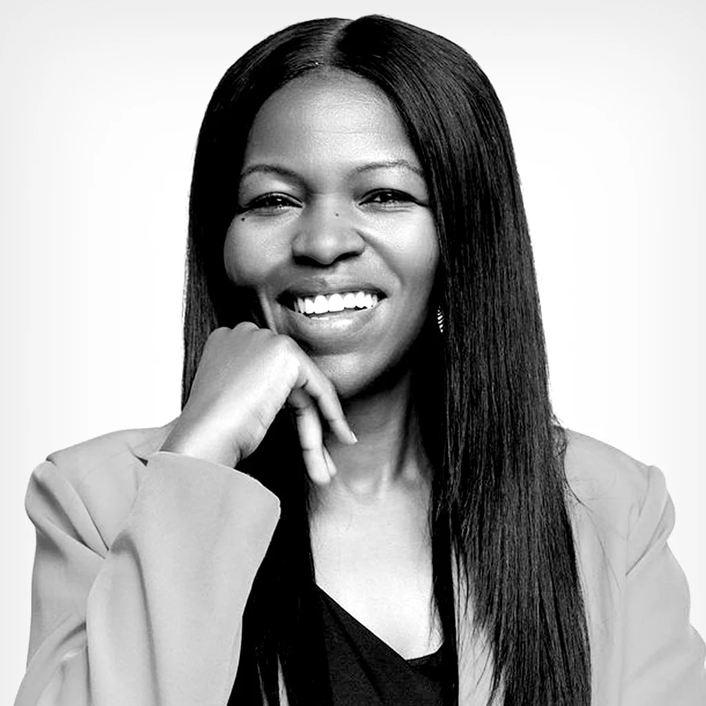 Black and white portrait of a woman smiling with her hand resting on her chin, wearing a blazer and earring.