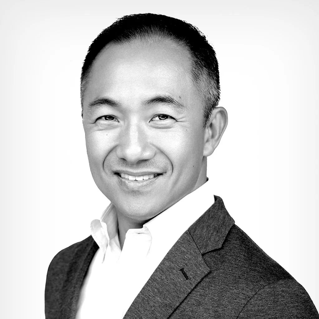 A black and white portrait of a smiling Asian man in a suit and white shirt.