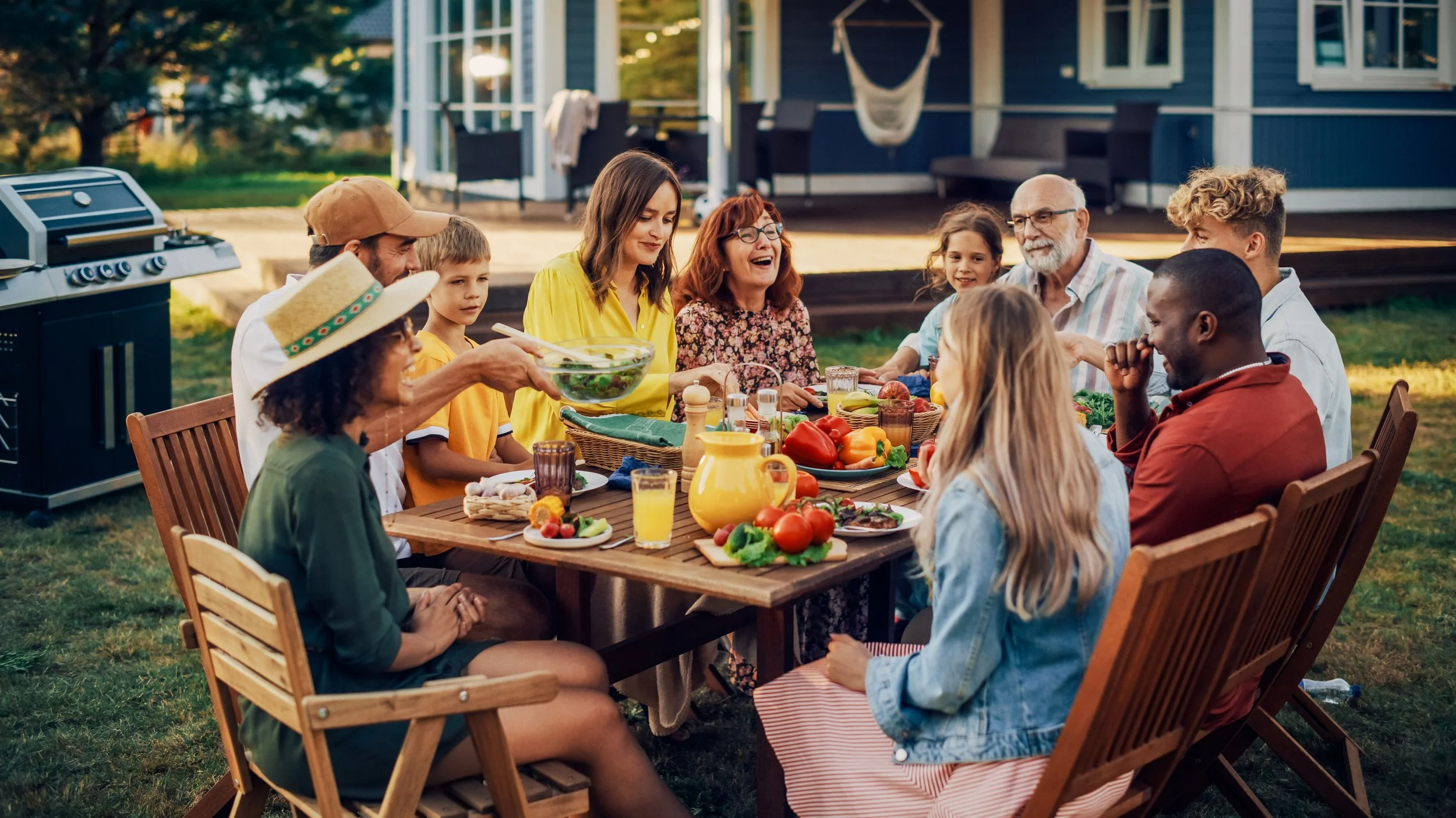 Multigenerational family having dinner with diverse friend group at a home backyard.