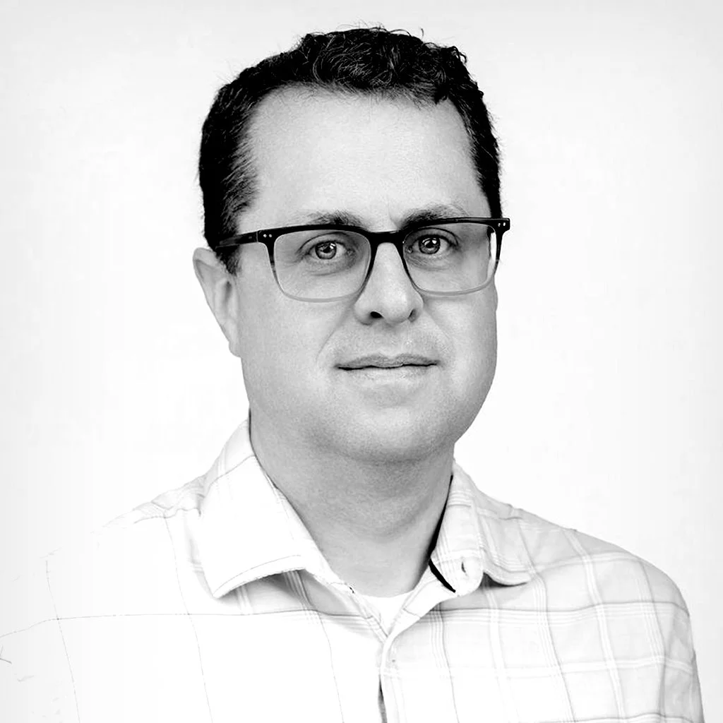 Black and white portrait of a man with glasses, short dark hair, wearing a collared shirt, facing forward.