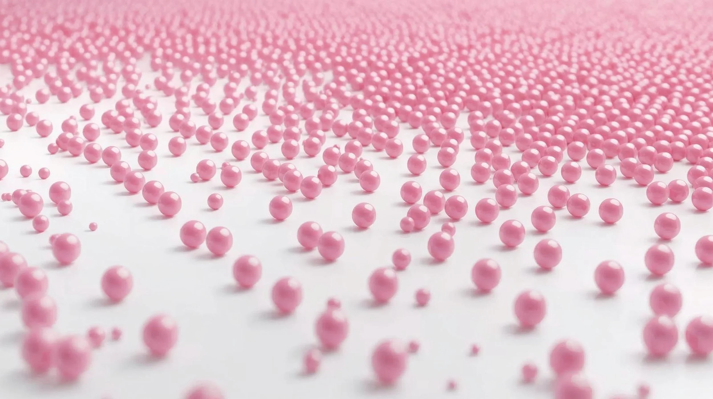 A large number of small pink beads scattered on a white surface, with more beads visible in the background.