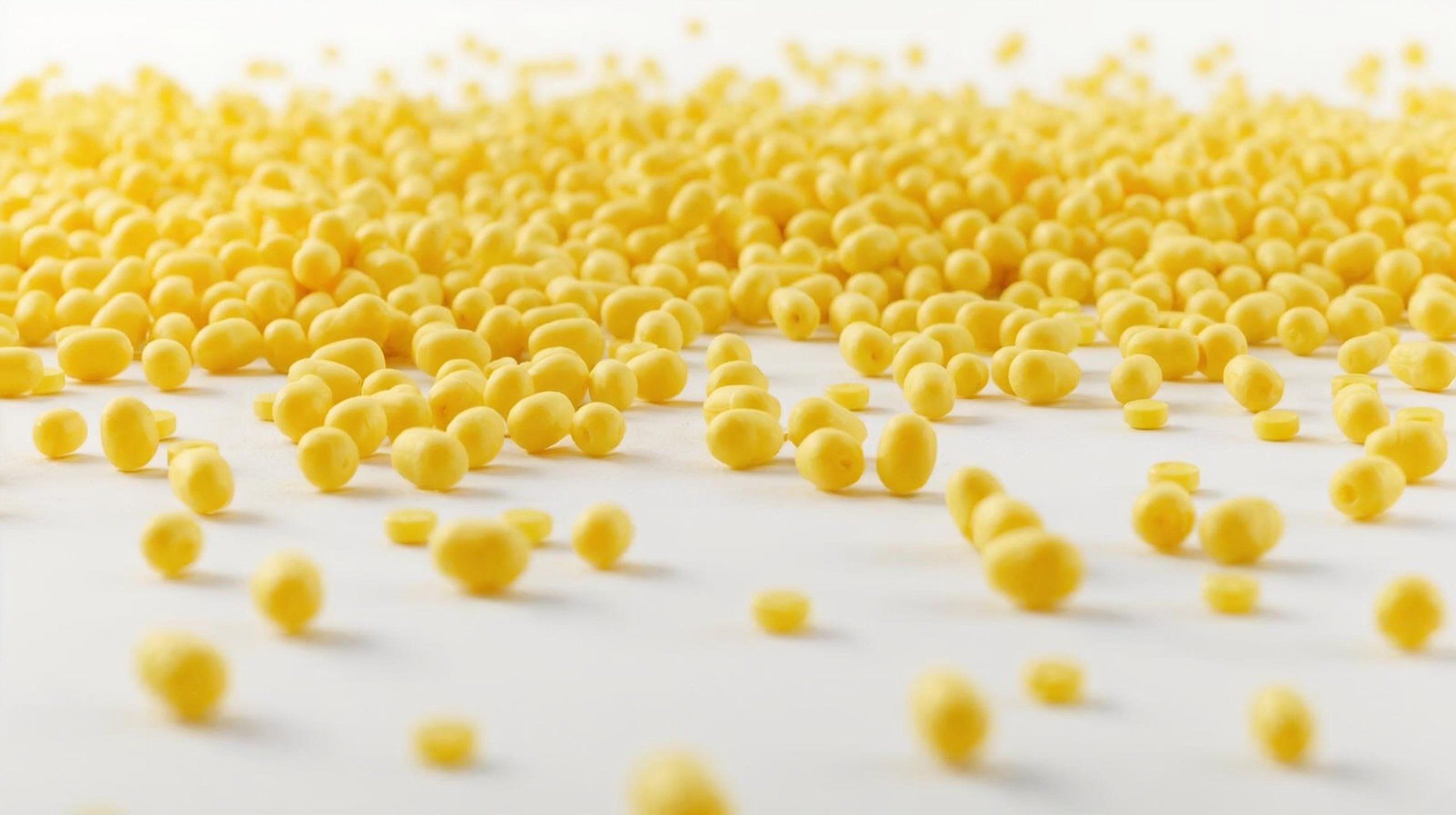 Yellow small spherical pasta scattered on a white surface with a blurred background.