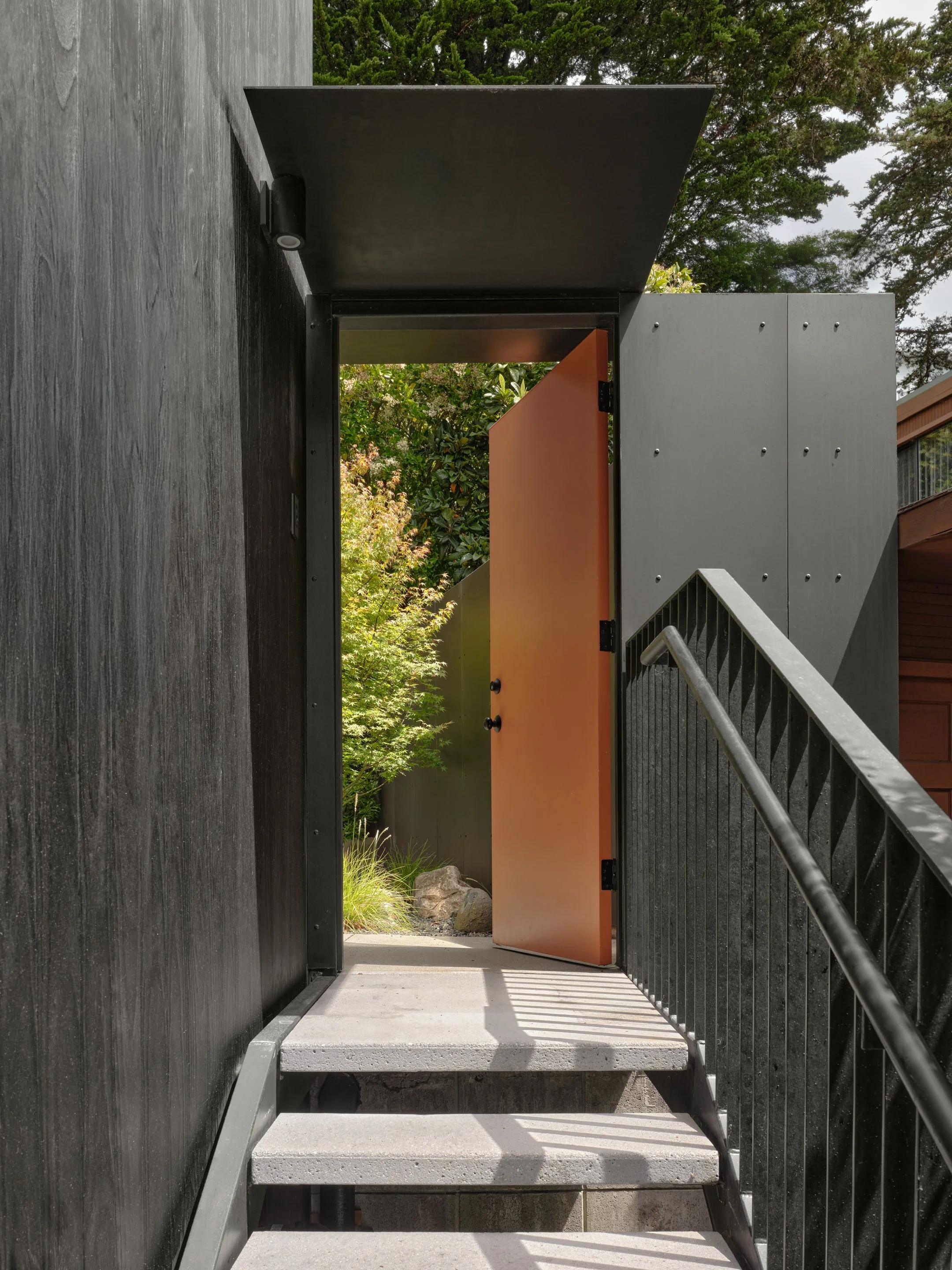 View through an open door on a staircase leading outside, with greenery and rocks visible beyond.