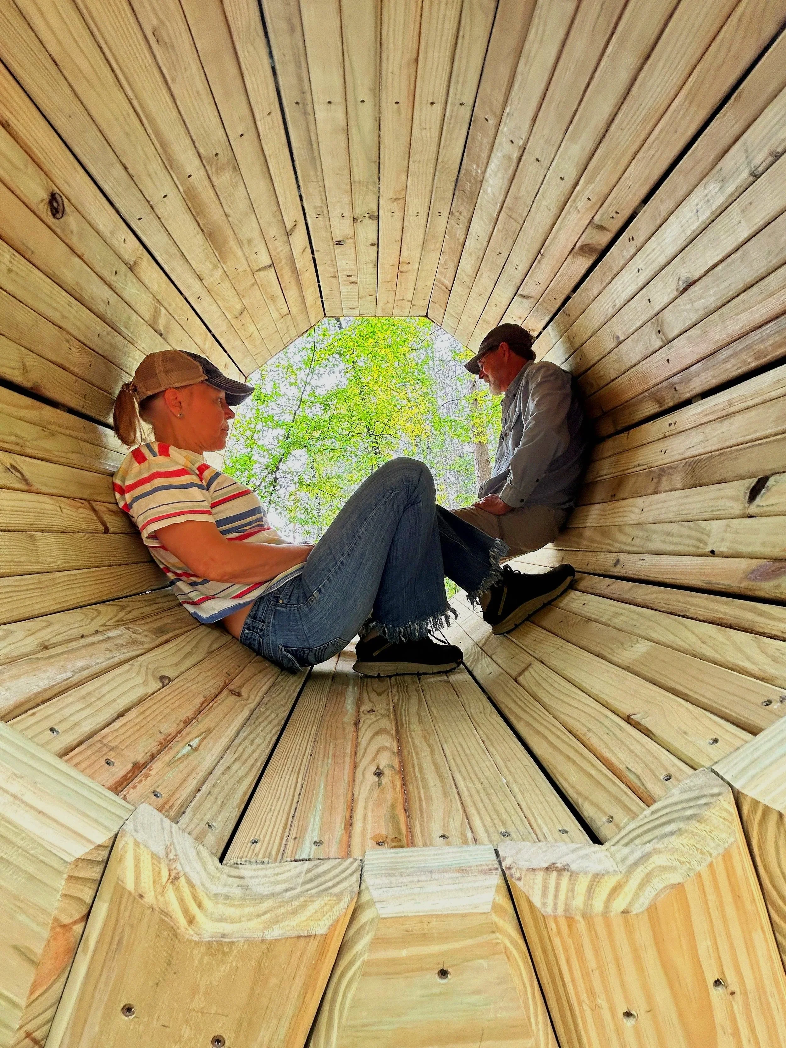 Two people sit inside the ten foot tall wooden forest megaphone.