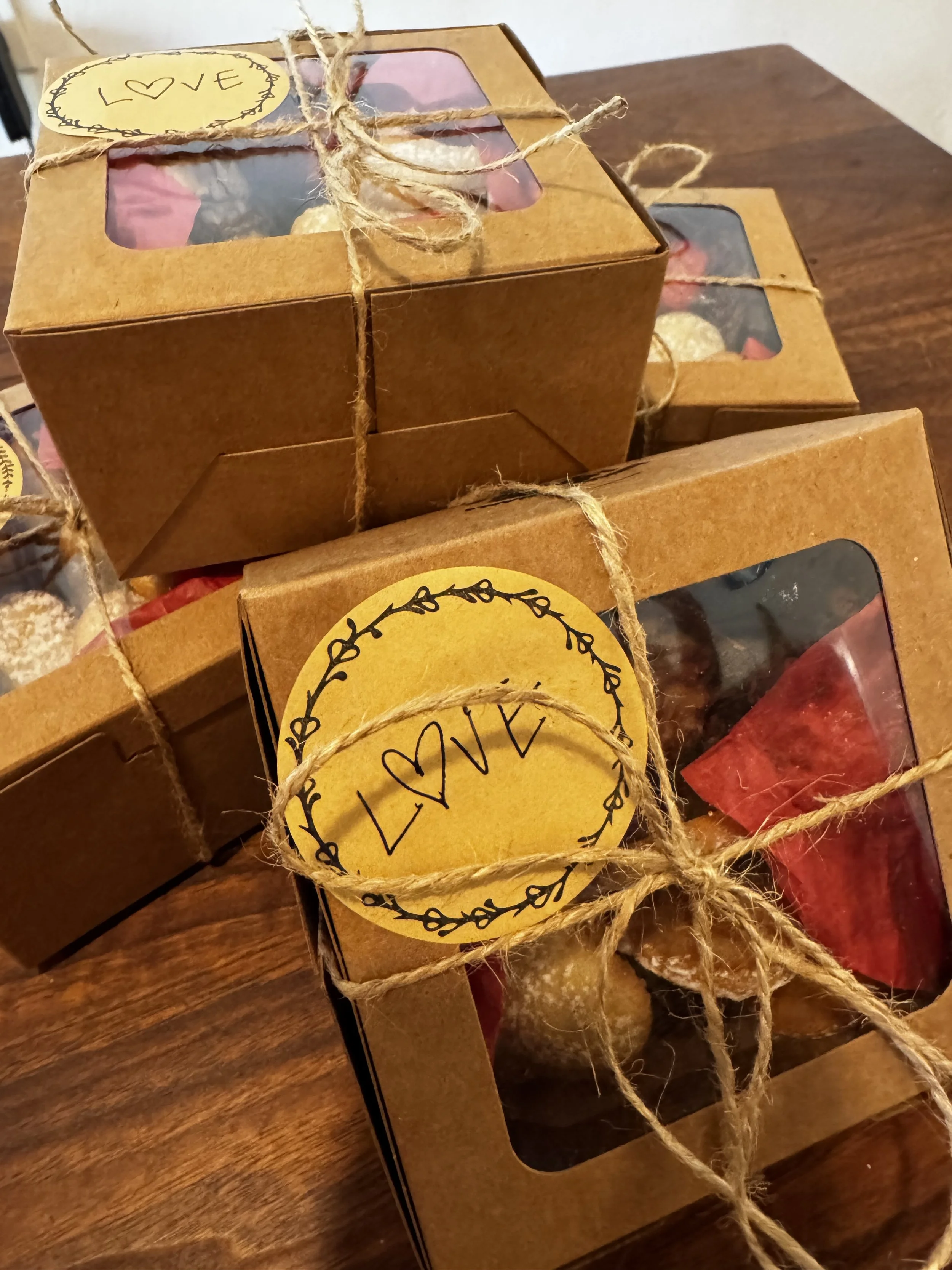 Gift boxes with clear windows showing assorted chocolates, tied with twine and decorated with yellow tags that say 'LOVE' and 'LOVE' with hearts.