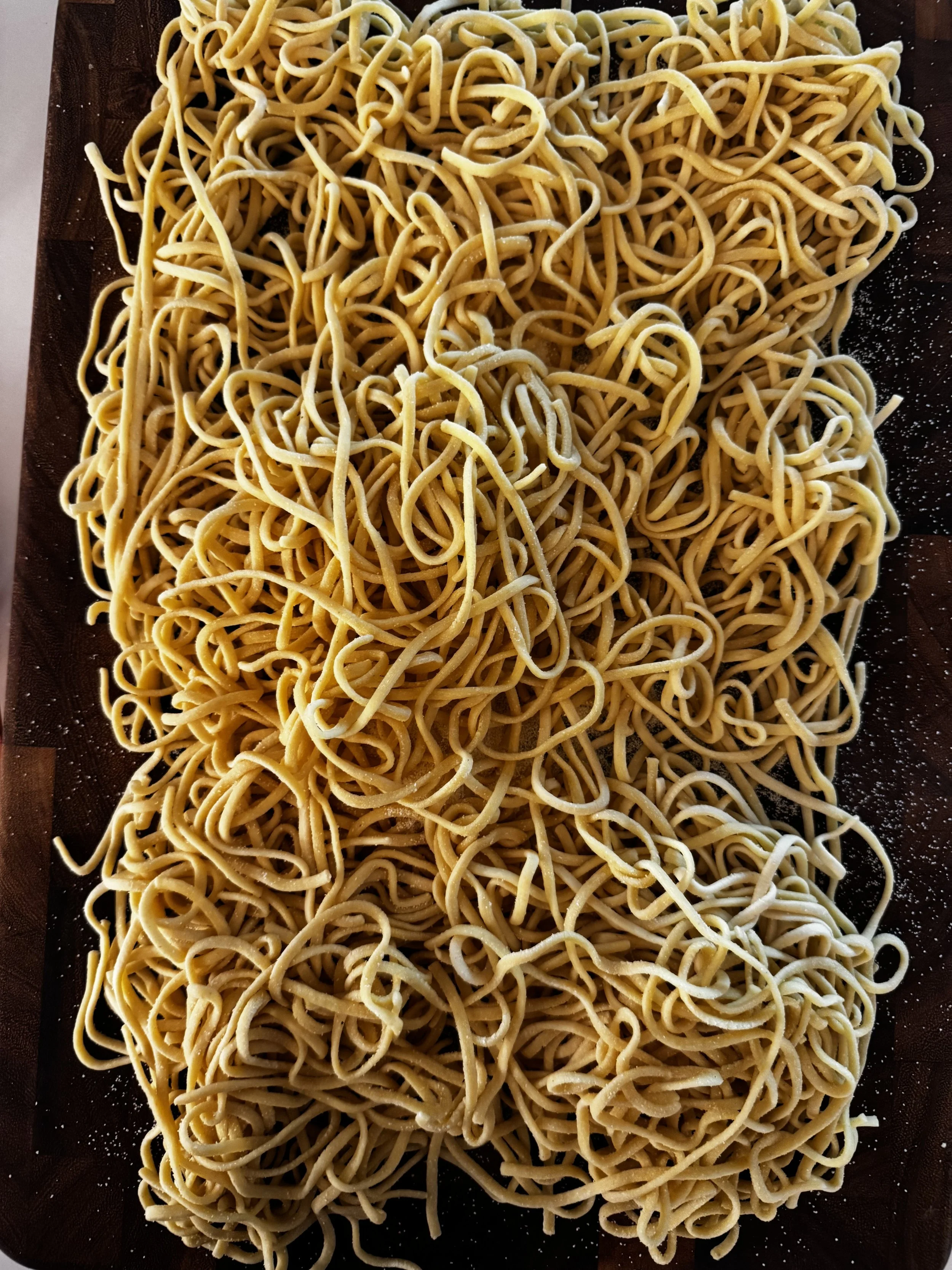 Uncooked yellow spaghetti noodles spread over a dark wooden surface.