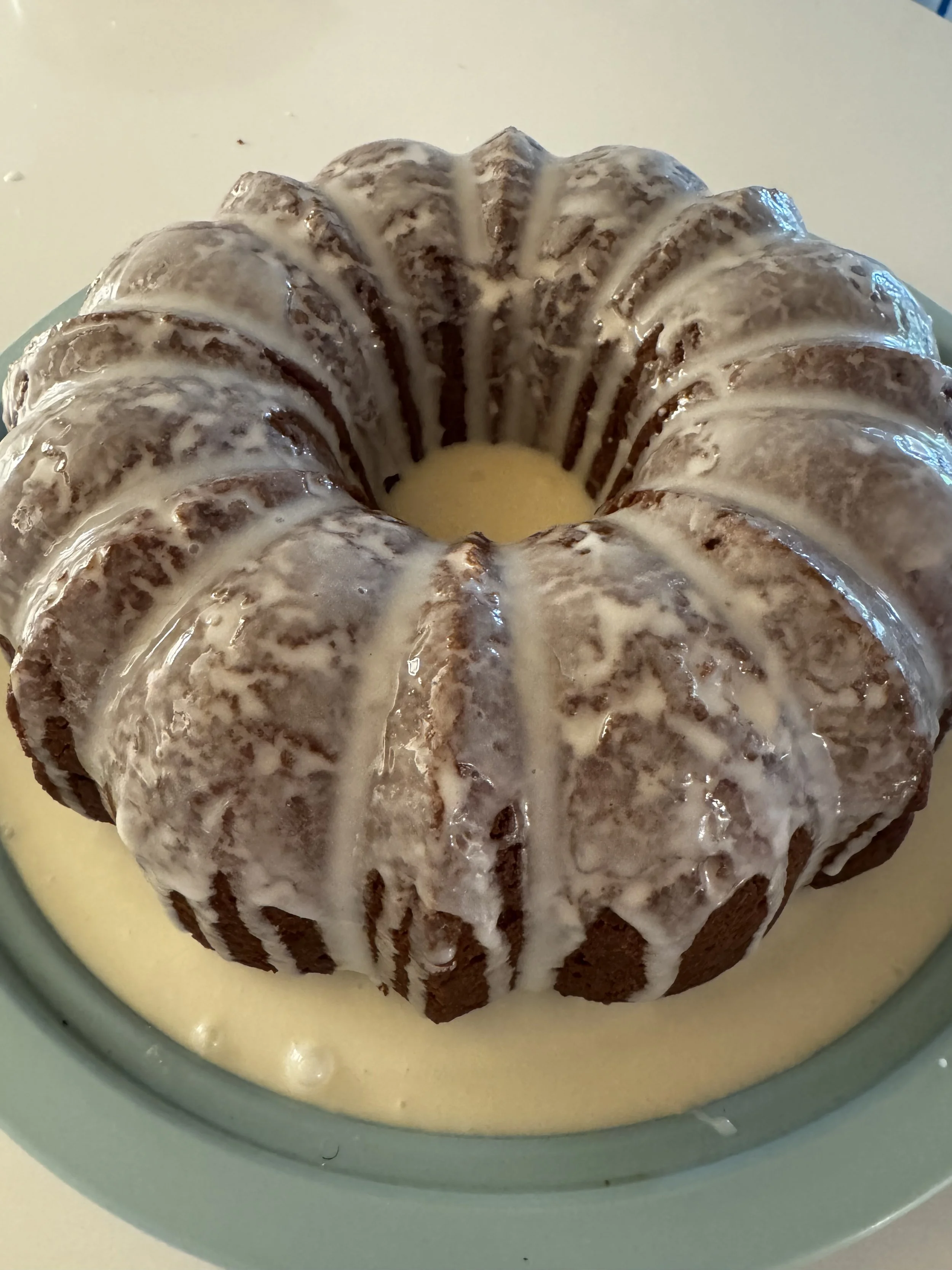 A Bundt cake with white icing drizzled over it, placed in a light green bowl filled with a creamy yellow sauce.