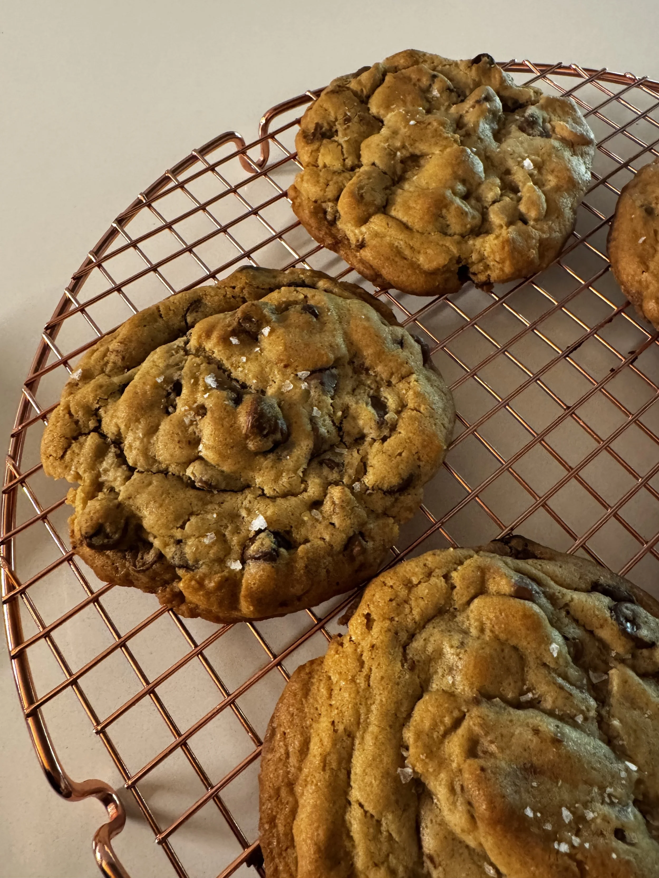 Three chocolate chip cookies on a copper cooling rack.