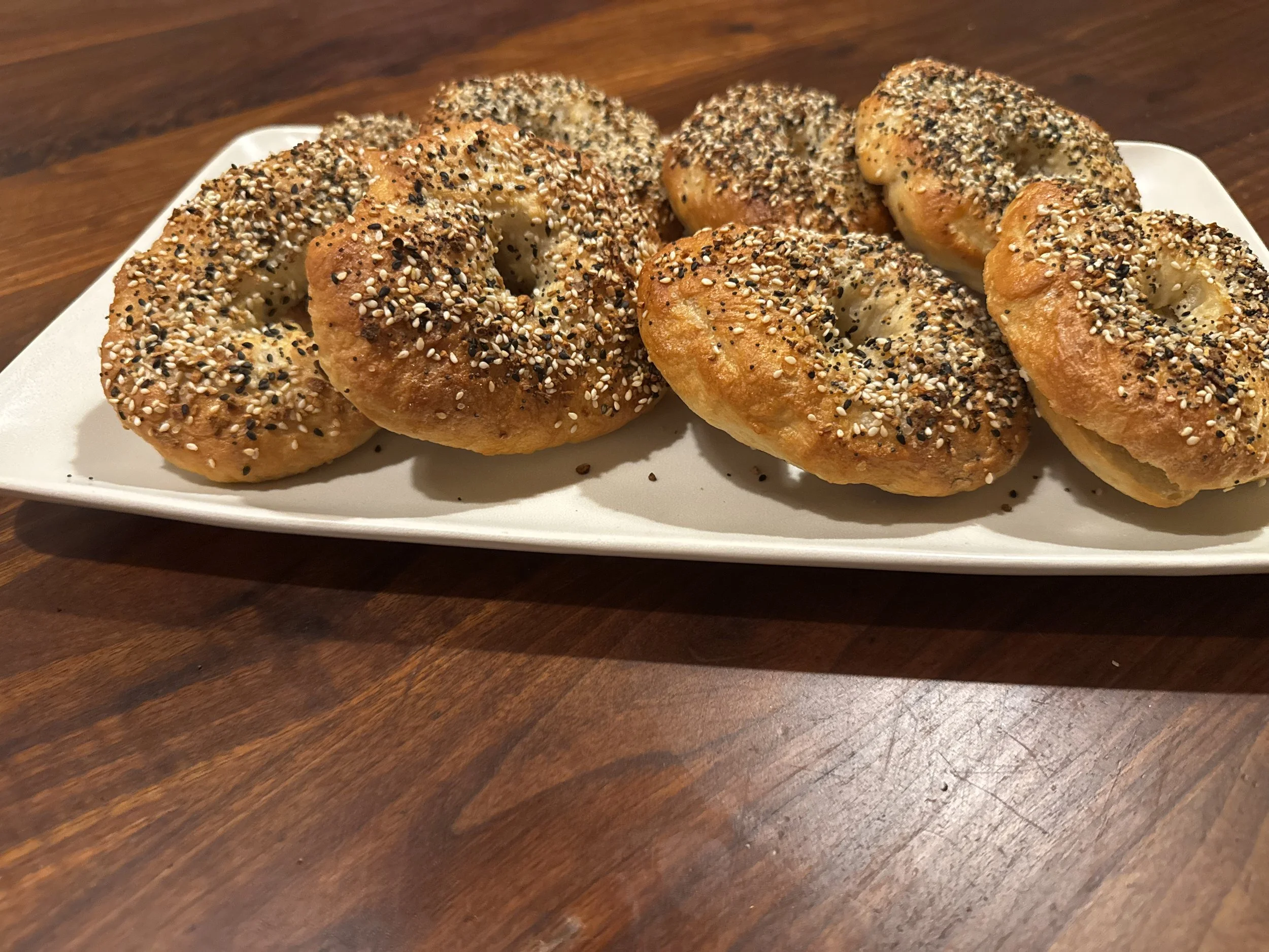 Four bagels topped with sesame, poppy, and black sesame seeds on a white rectangular plate.