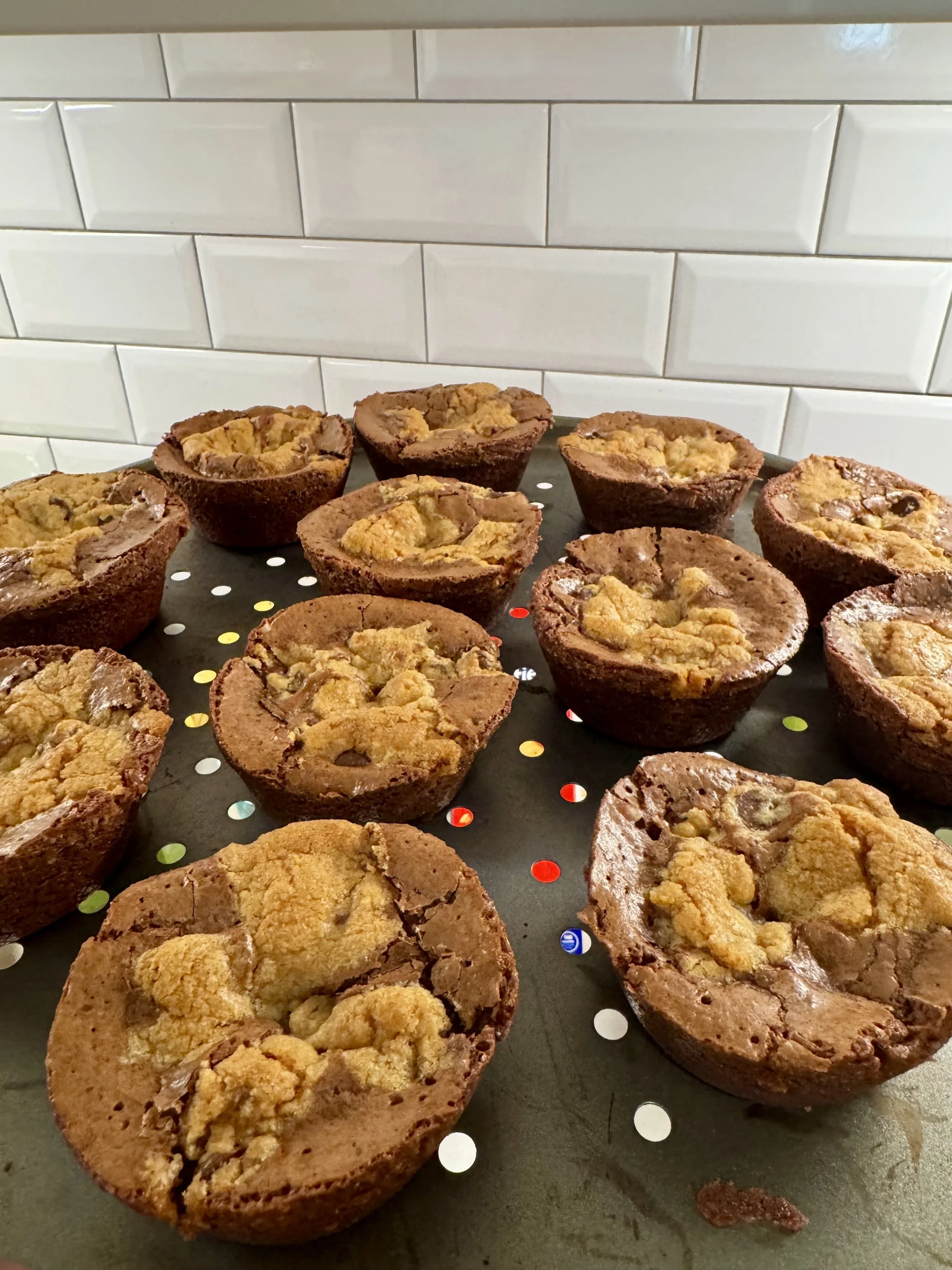 Chocolate chip cookies placed on a perforated baking sheet with a white subway tile backsplash in the background.