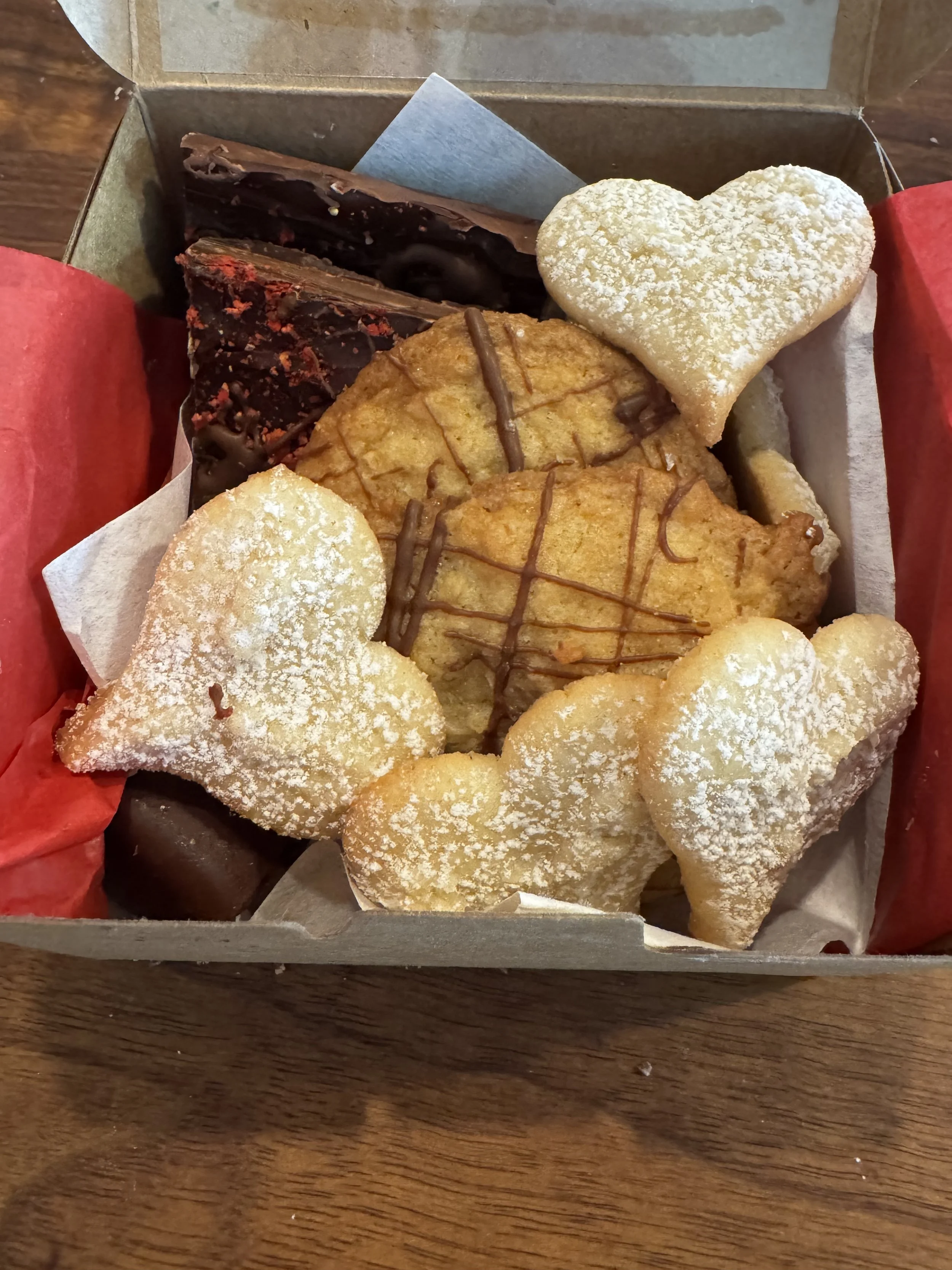A box of assorted cookies including heart-shaped, chocolate-drizzled, and chocolate-covered treats.