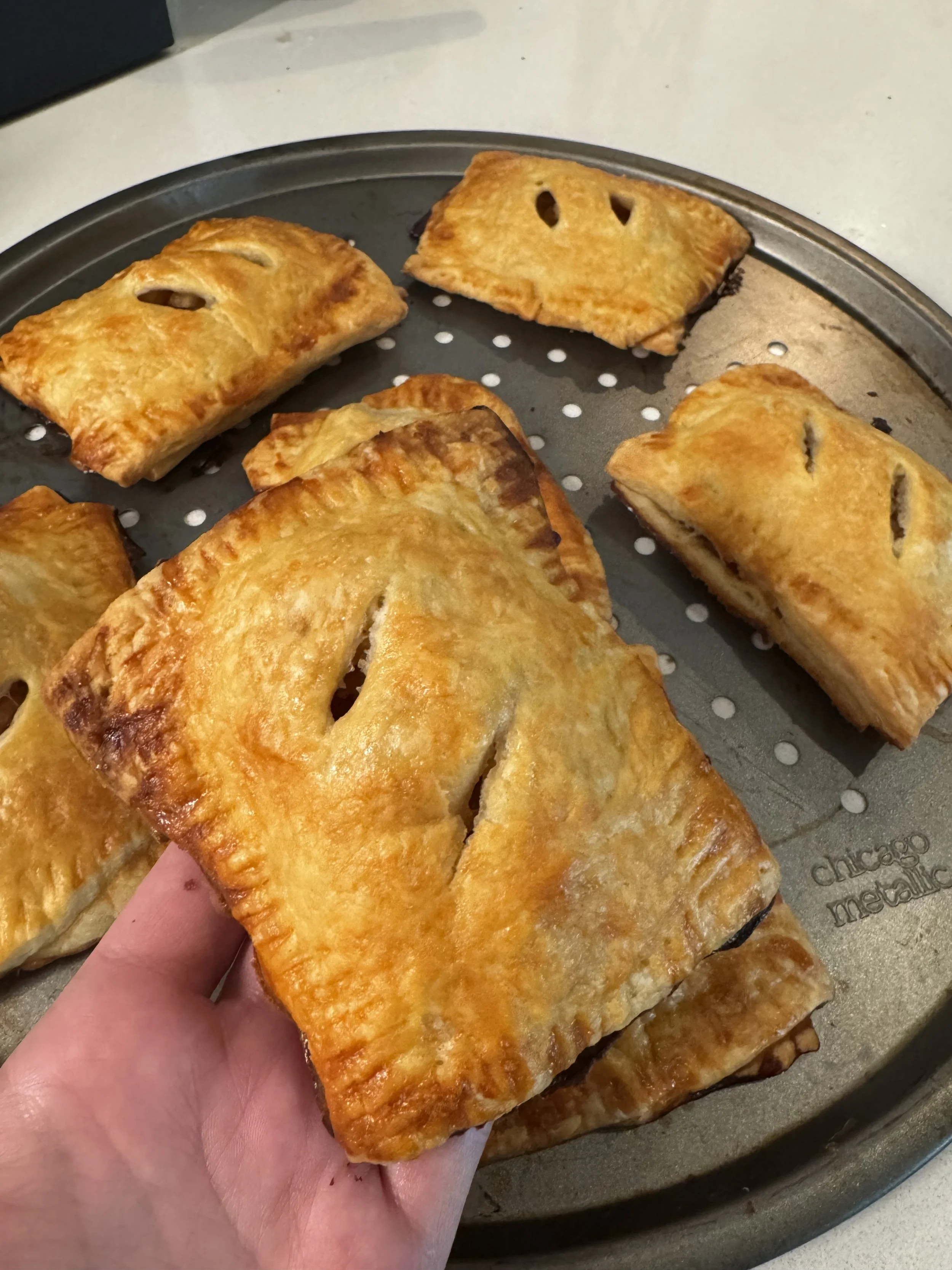 Baked empanadas on a baking sheet, with one held in hand showing the golden-brown crust.