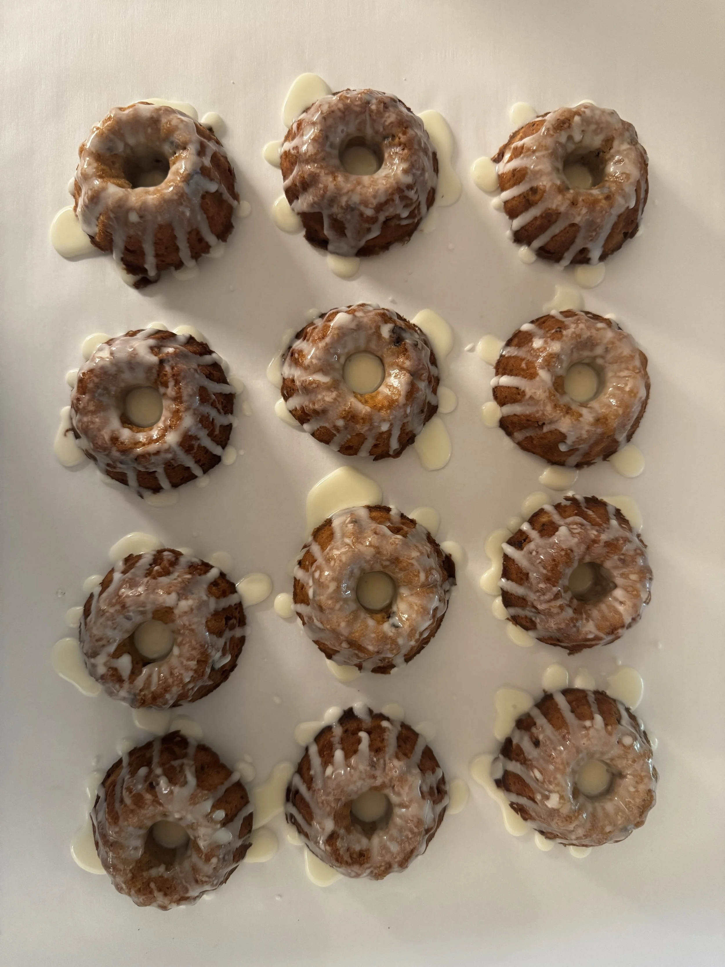 A white tray with twelve mini bundt cakes topped with a white glaze and drizzled with additional glaze.